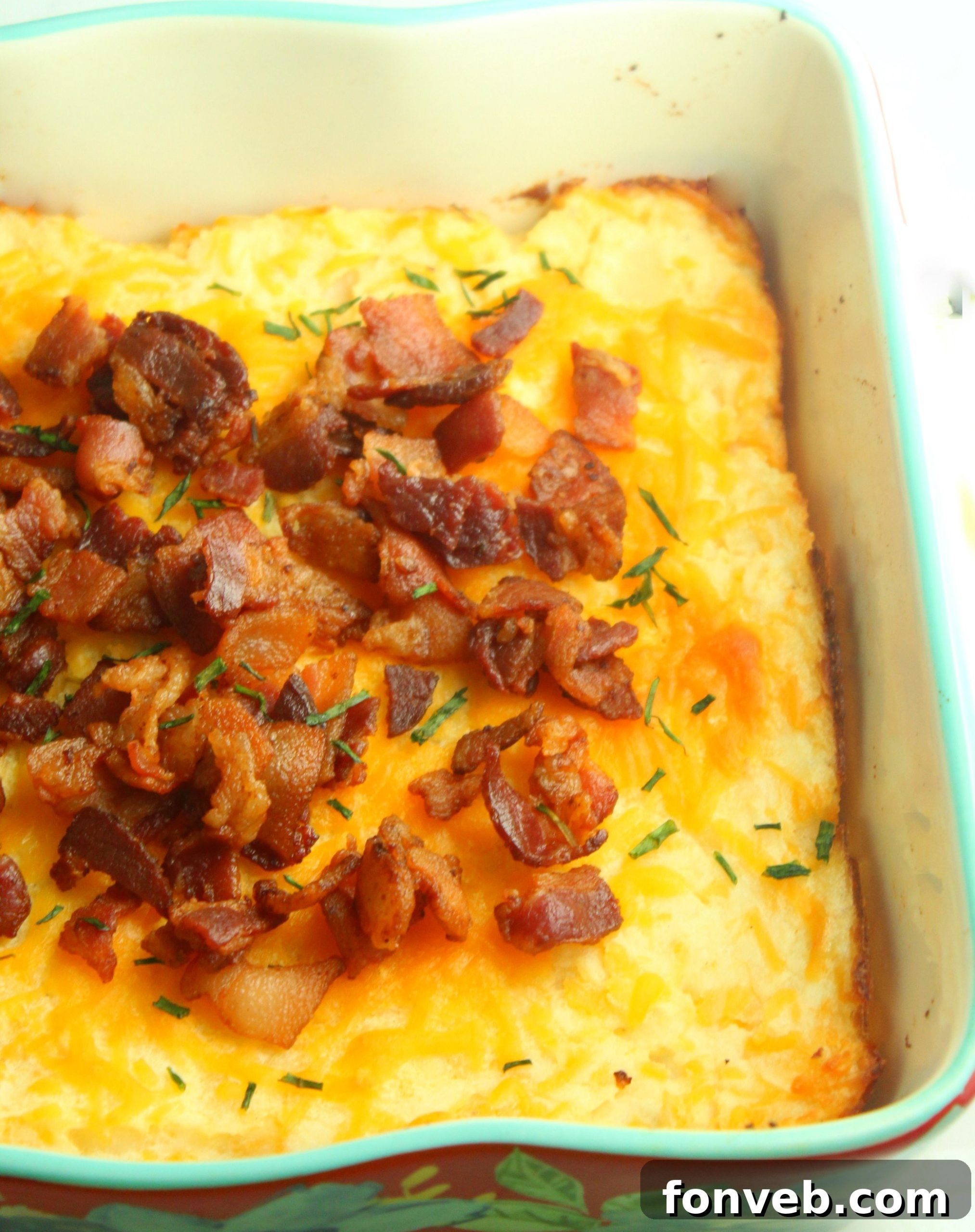 Ultimate Loaded Potato Bake 3 A dish of loaded mashed potato casserole with a scoop taken out, revealing its creamy texture and cheesy layers, garnished with bacon and green onions.