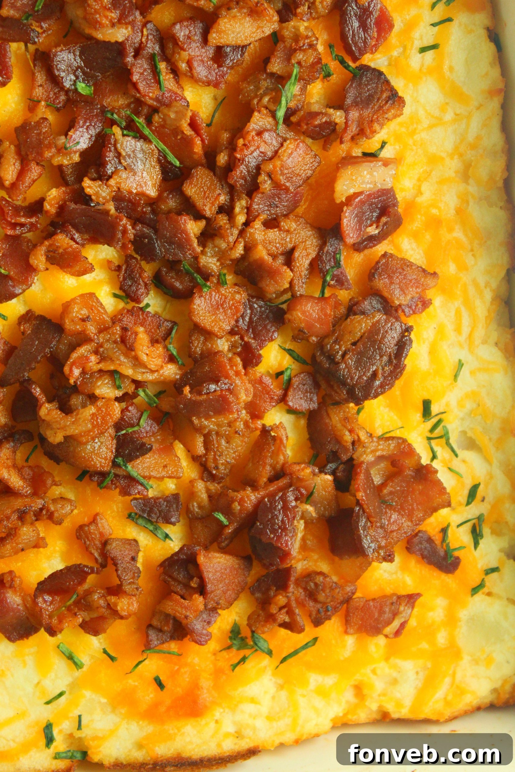 Ultimate Loaded Potato Bake 4 Overhead shot of a full dish of loaded mashed potato casserole, with melted cheese, crispy bacon, and chopped green onions on top.