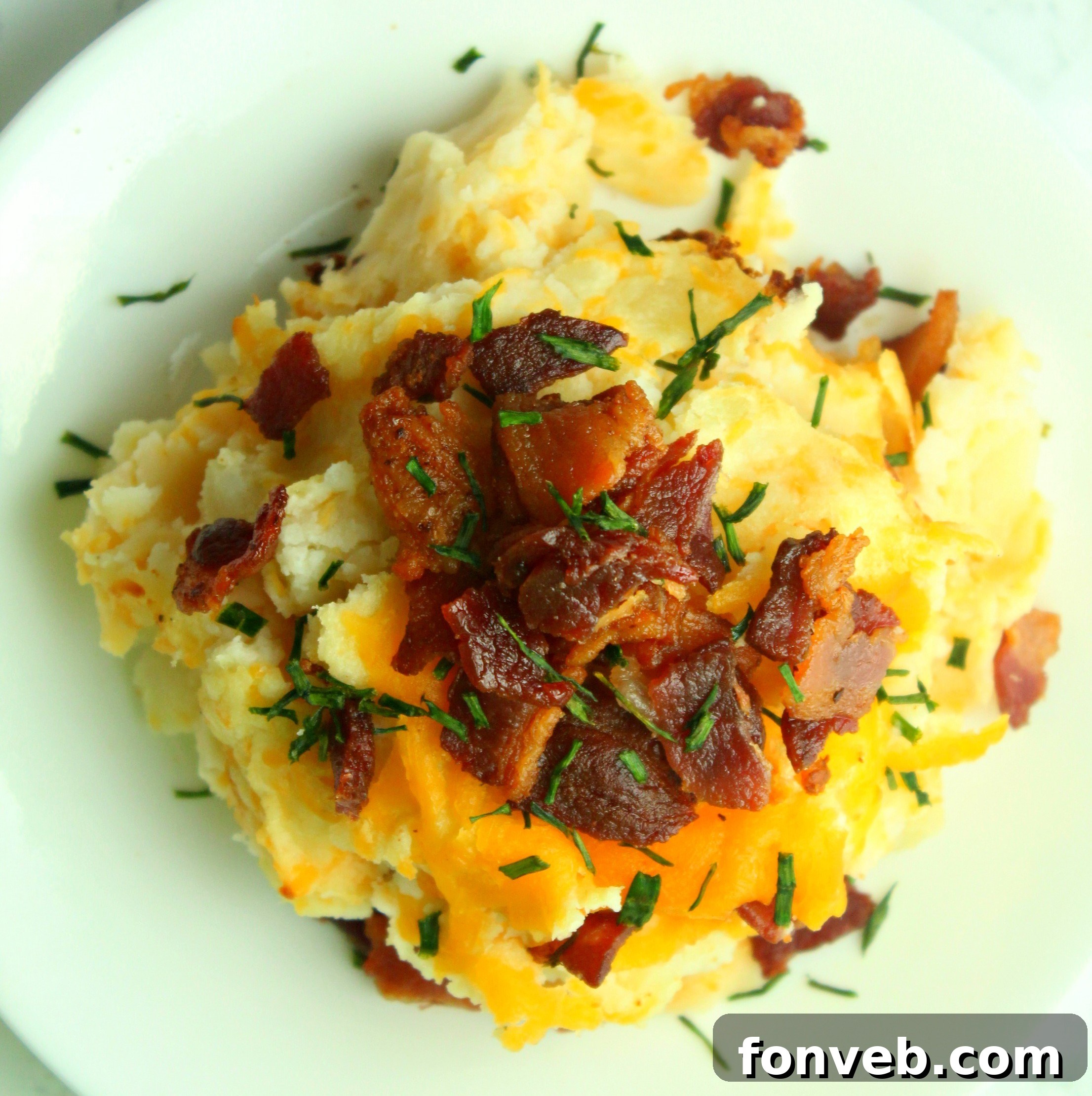 Ultimate Loaded Potato Bake 5 A close-up of the loaded mashed potato casserole, showing the bubbling cheese, crispy bacon bits, and vibrant green onions.