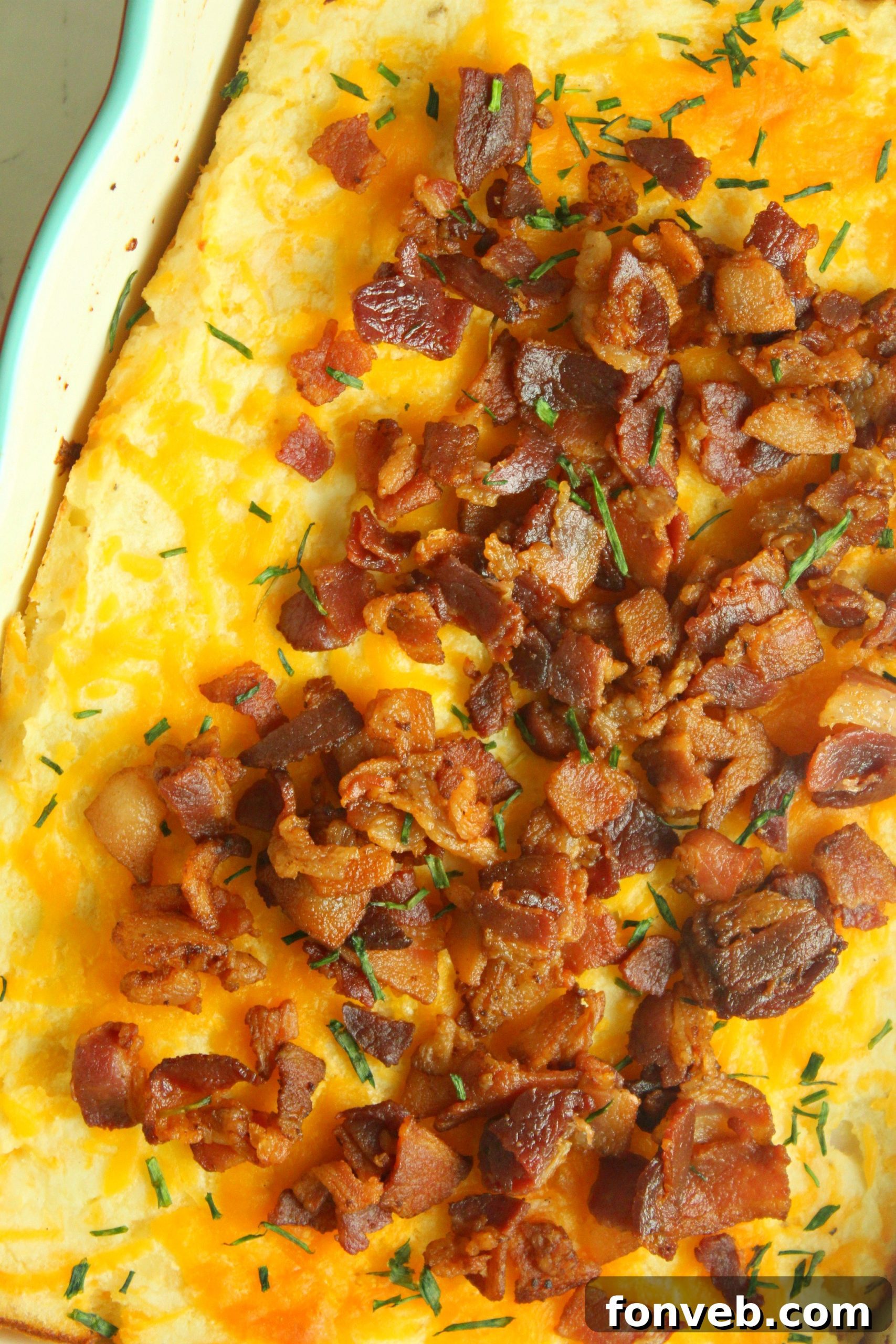 Ultimate Loaded Potato Bake 8 A serving of loaded mashed potato casserole on a plate, garnished with more fresh green onions and bacon bits.