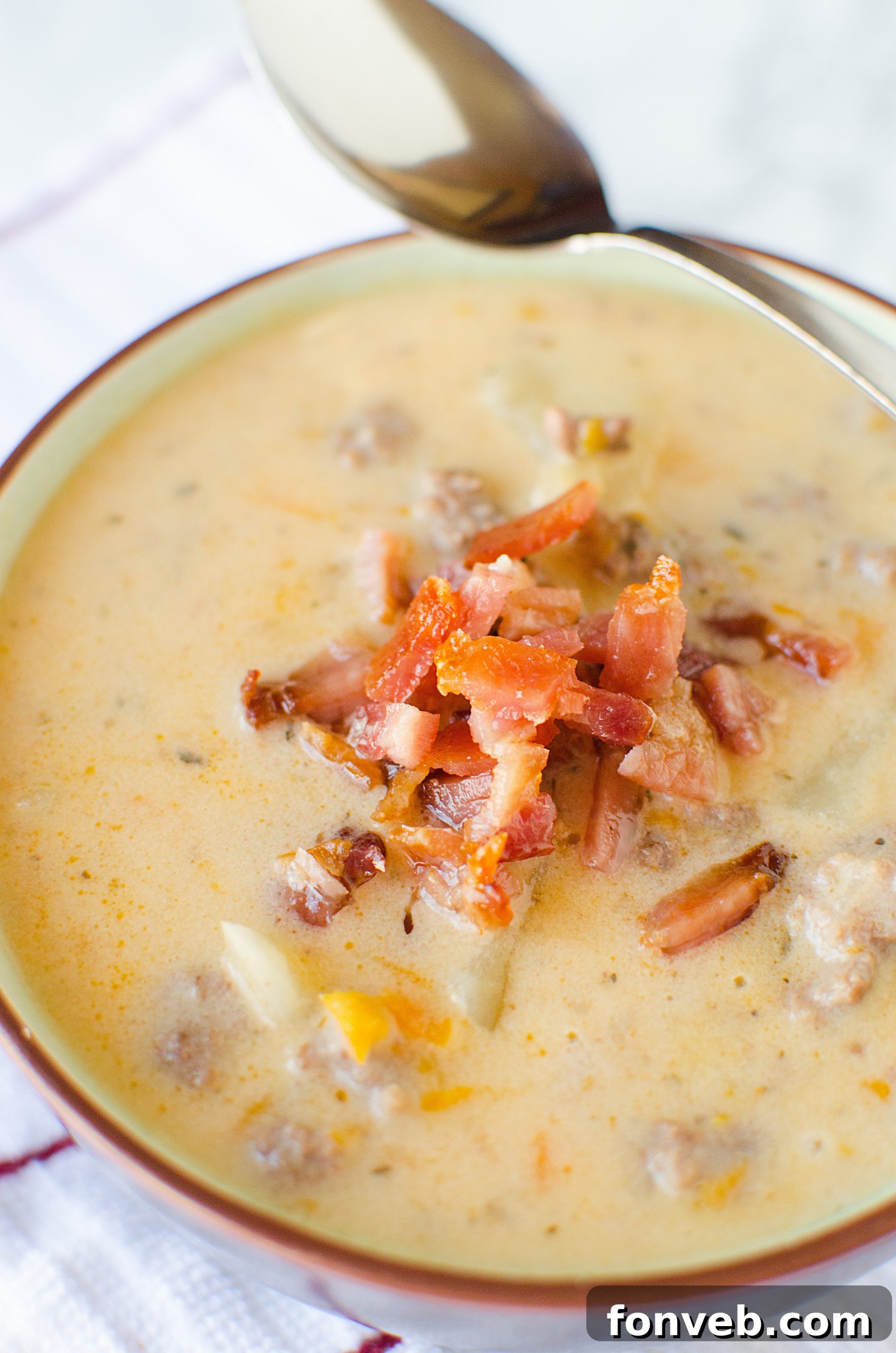 A close-up shot of a steaming bowl of Slow Cooker Cheeseburger Soup, garnished with fresh chives, showing its rich, creamy texture and chunks of ground beef and potatoes.
