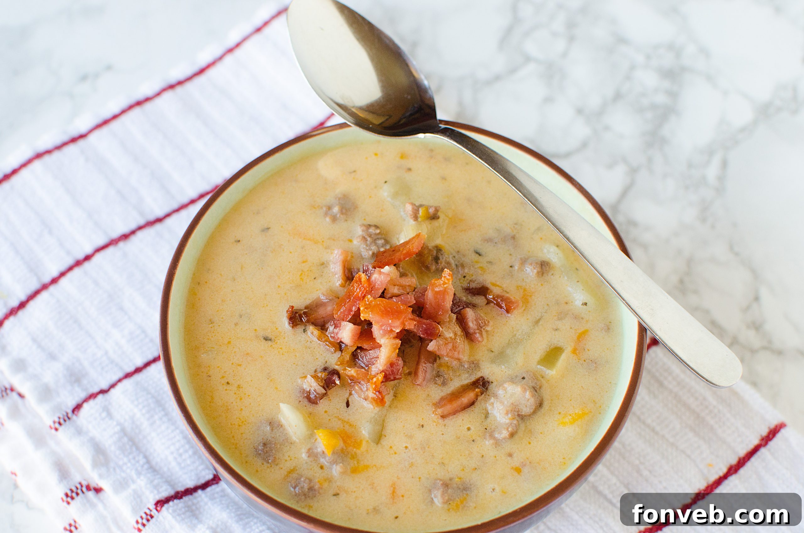 An aerial view of Slow Cooker Cheeseburger Soup simmering in a crock pot, showcasing the various ingredients like diced potatoes, carrots, and ground beef, ready to be combined with dairy.