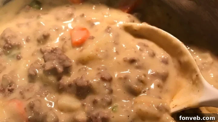 A close-up of a serving spoon scooping up creamy Slow Cooker Cheeseburger Soup, highlighting the rich cheese and tender ground beef, with a focus on its appetizing texture.