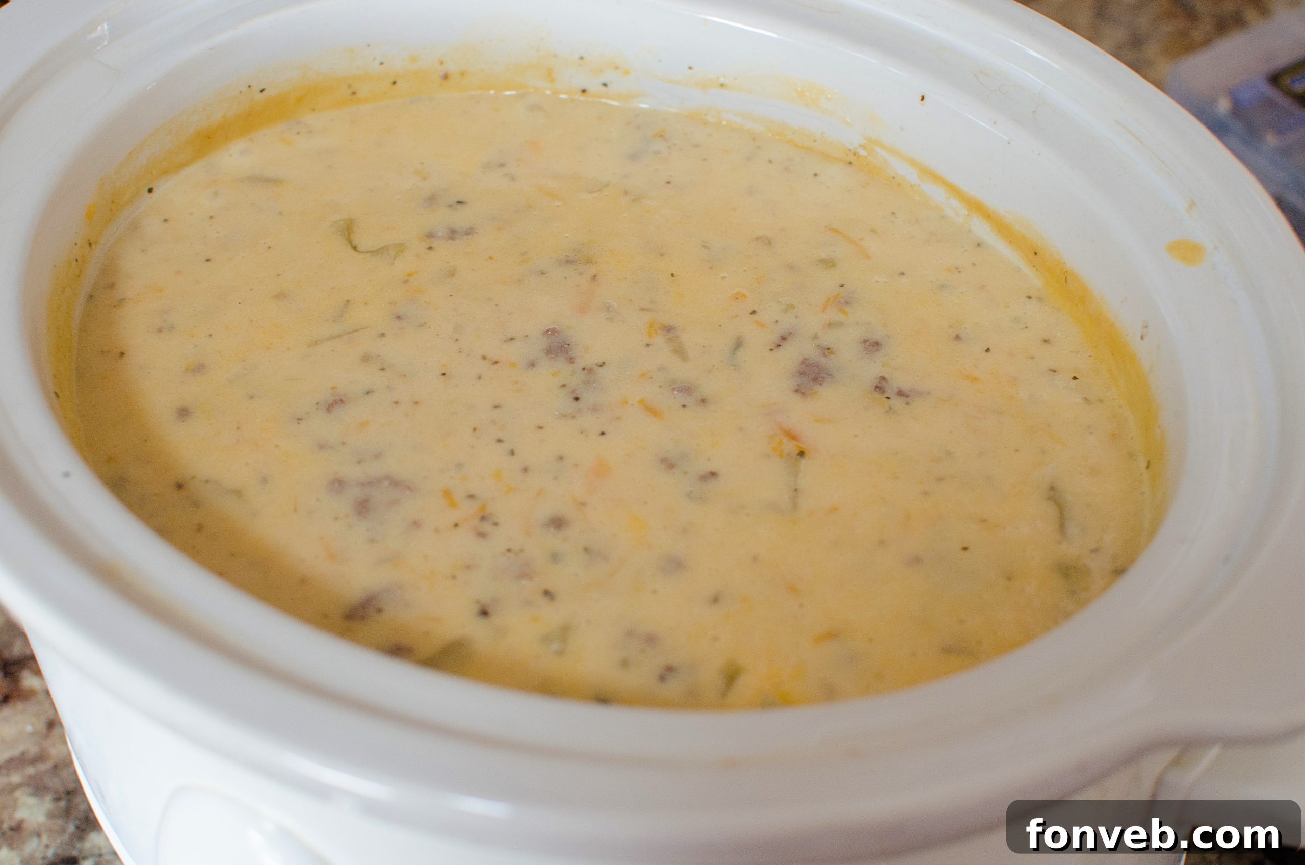 Two hands holding a rustic bowl of Slow Cooker Cheeseburger Soup, accompanied by crusty bread on a wooden surface, emphasizing warmth and homemade goodness.