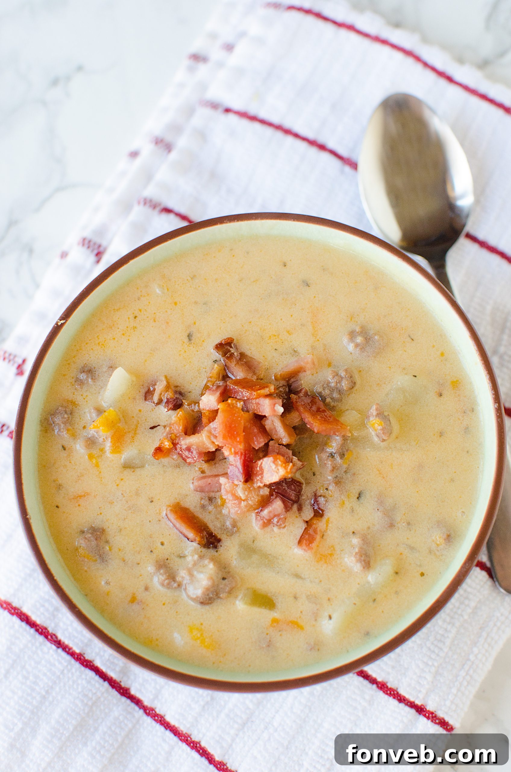 An overhead shot of Slow Cooker Cheeseburger Soup in a bowl, generously topped with crispy bacon bits and chopped green onions, ready for serving.