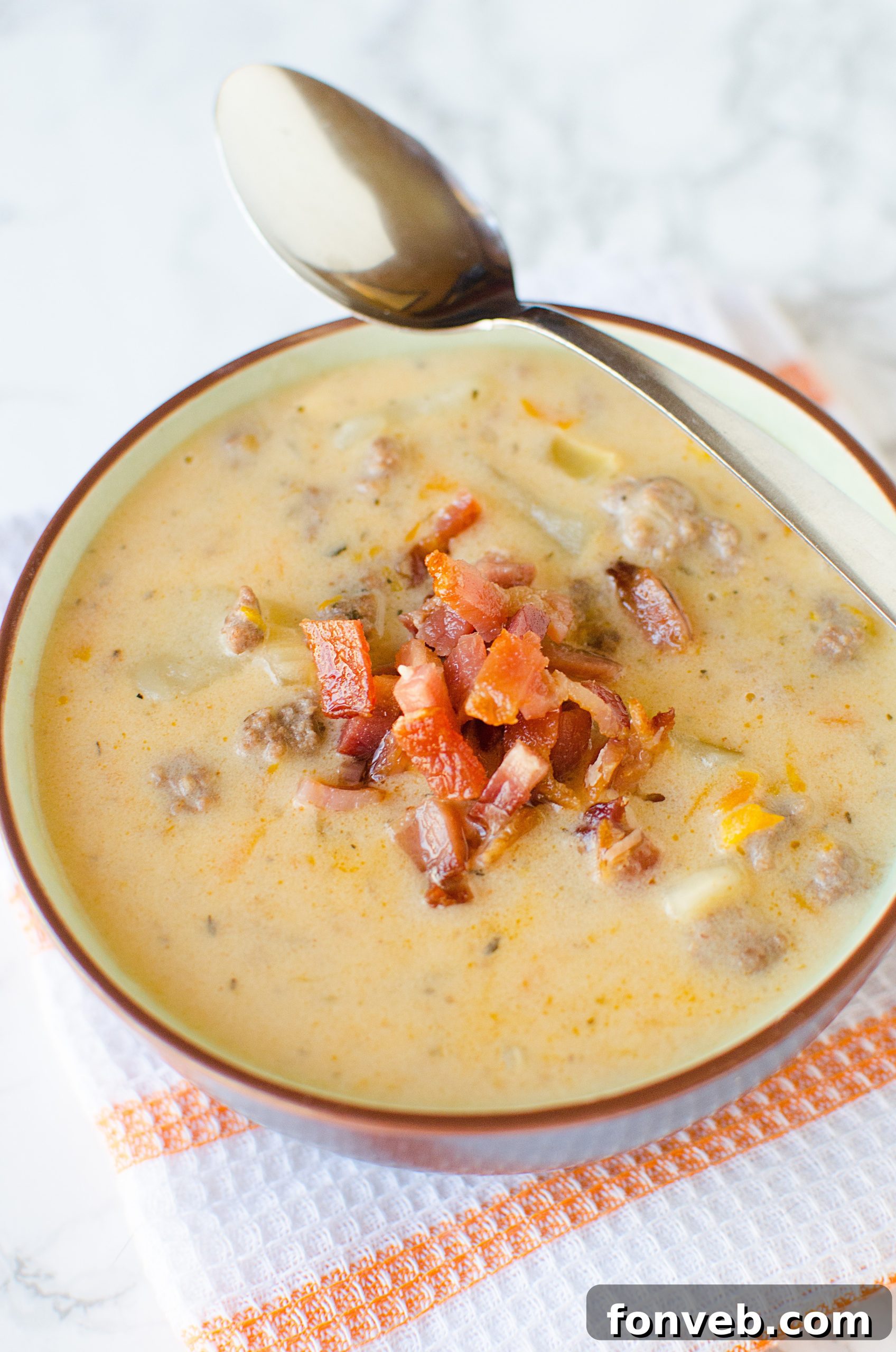 A beautifully composed flat lay of Slow Cooker Cheeseburger Soup, showcasing its texture and rich color, with rustic kitchen elements in the background.
