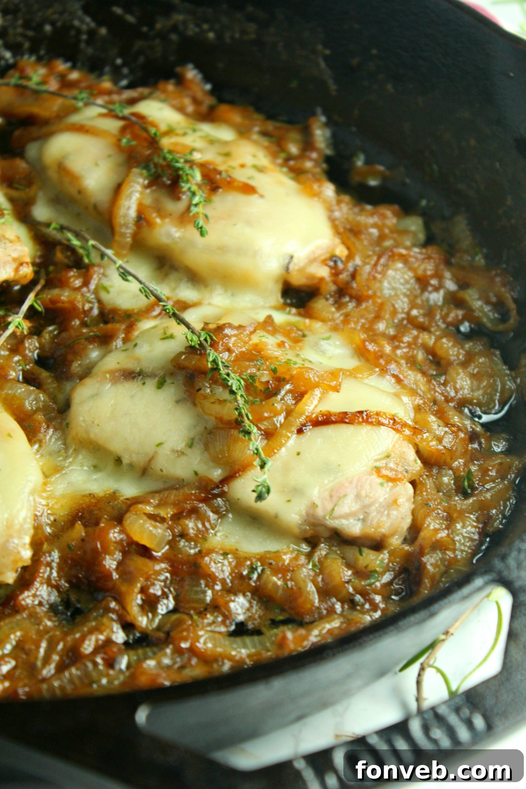 Closeup of cooked smothered French onion pork chops in a skillet, cheese bubbling, fresh thyme garnish