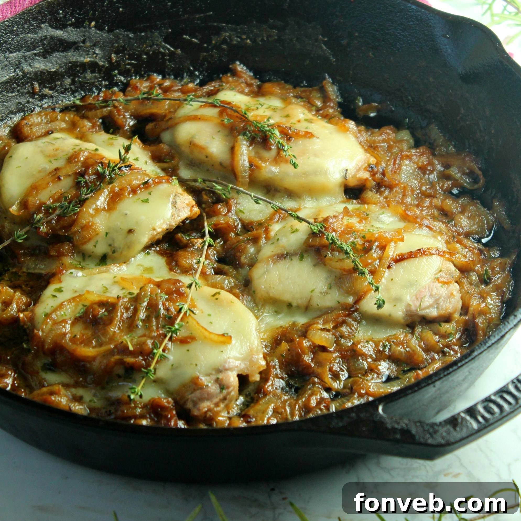 Smothered French onion pork chops simmering in a pan, steam gently rising, highlighting the savory goodness