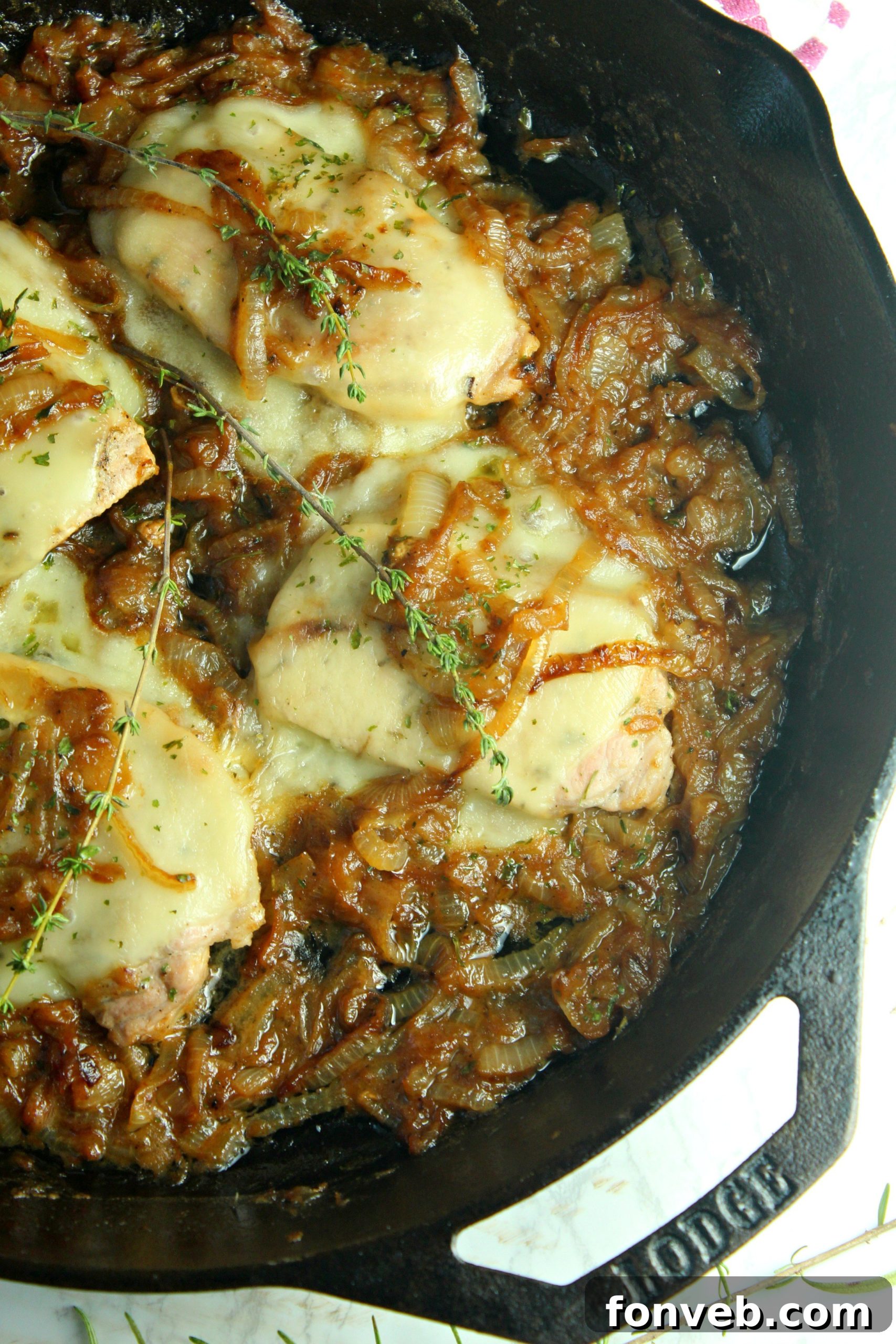 A chef's hand garnishing a plate of smothered French onion pork chops with fresh thyme sprigs before serving