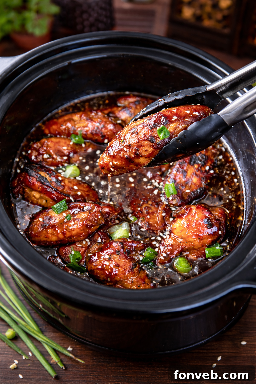 Slow Cooker Teriyaki Wings in a slow cooker with tongs lifting one up, showcasing its tenderness