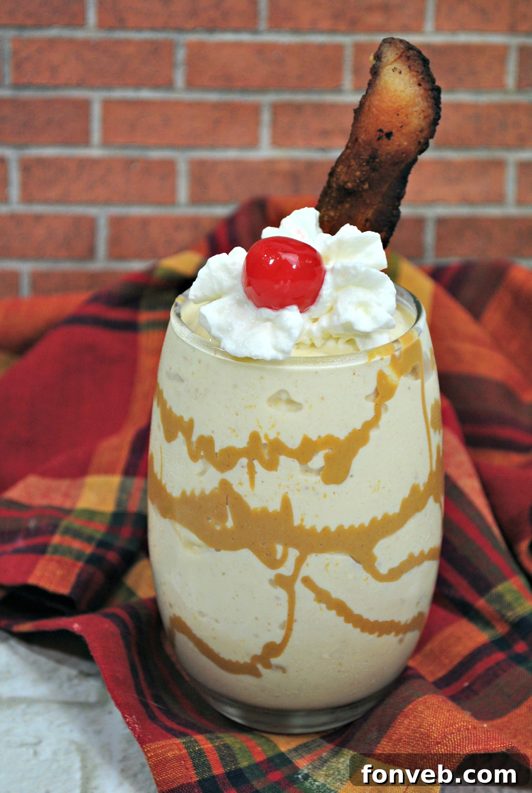 A close-up of the Dirty Elvis Cocktail, highlighting the texture and garnishes including whipped cream, a cherry, and bacon.