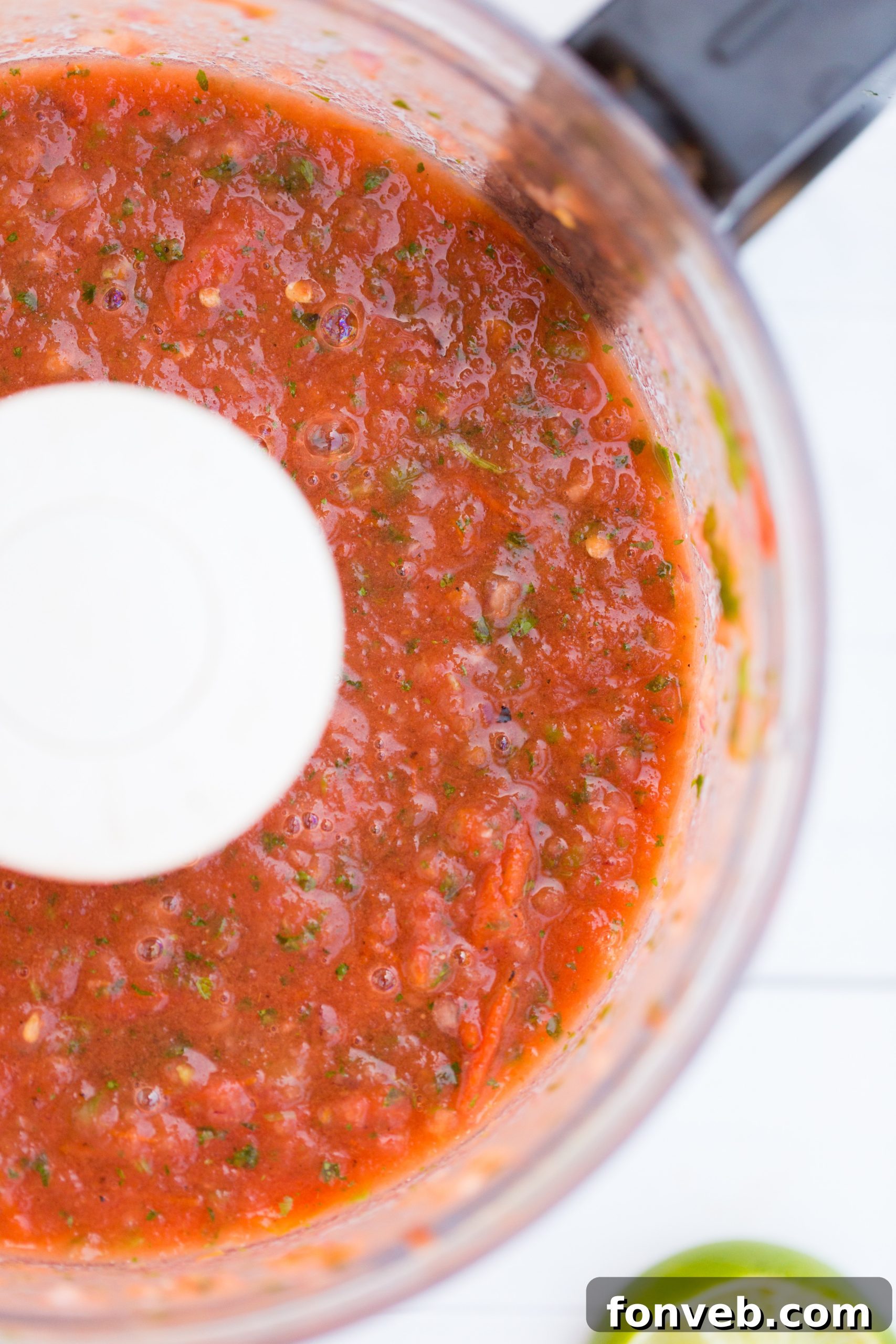 Signature Restaurant Salsa at Home 4 A food processor actively blending roasted Roma tomatoes, jalapeños, and other fresh aromatics into a rich red salsa mixture, showcasing the blending process.