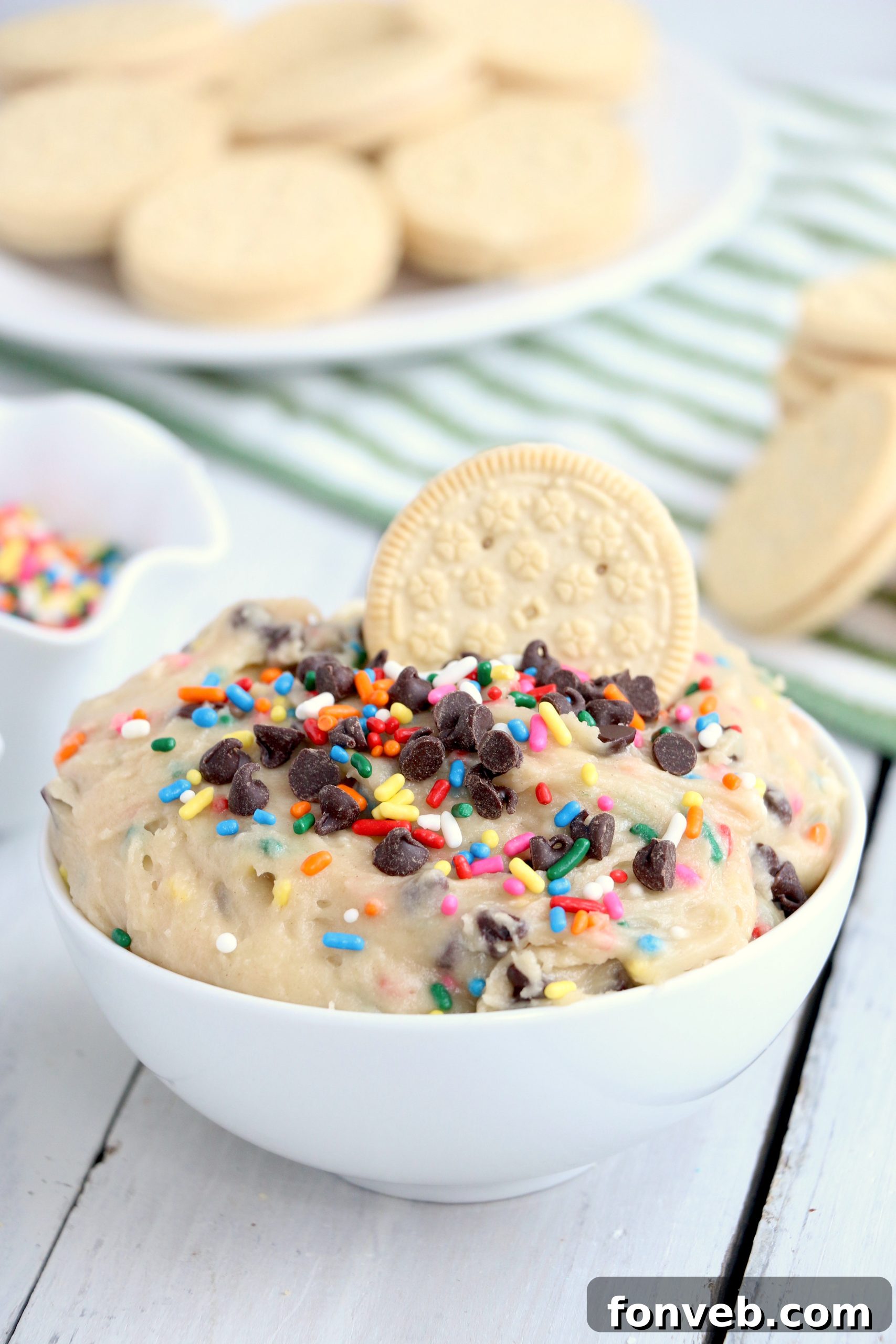 Close-up of a bowl of Funfetti Cookie Dough Dip with colorful sprinkles, surrounded by vanilla cookies for dipping.