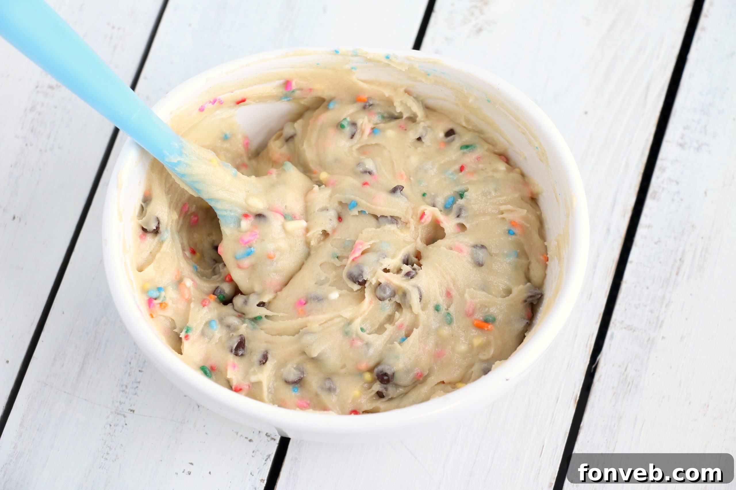 Close-up shot of a hand holding a vanilla cookie, dipping it into a bowl of Funfetti Cookie Dough Dip.