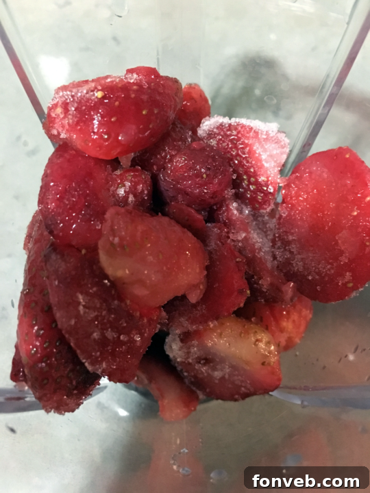 Frozen strawberries being added to a blender, the first step in making the milkshake.