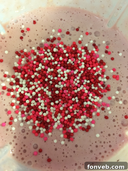 Two Strawberry White Chocolate Milkshakes garnished with whipped cream and sprinkles, ready to serve.