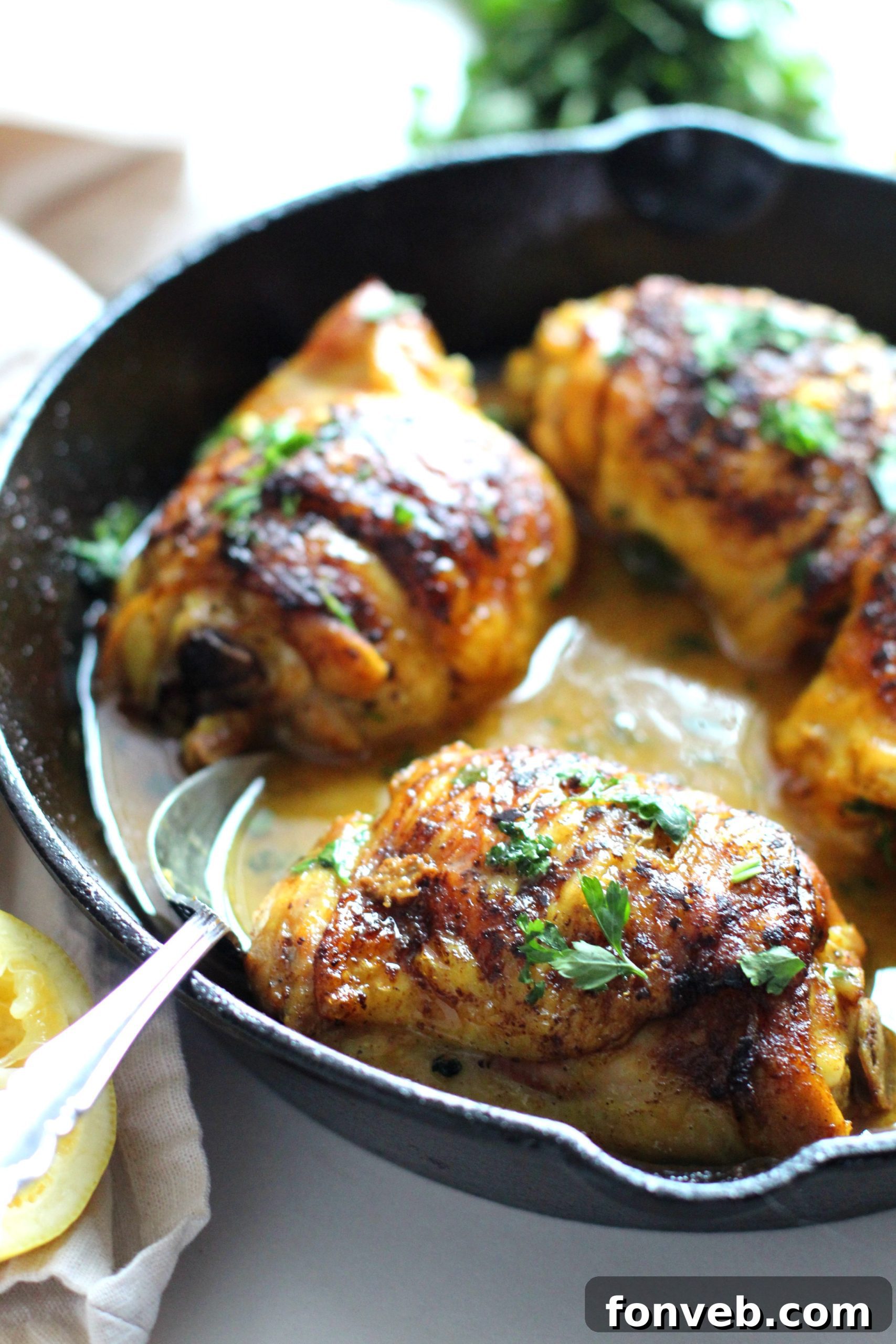 Golden brown pan-seared chicken thighs with lemon slices and fresh parsley in a cast iron skillet, ready to be served over rice.