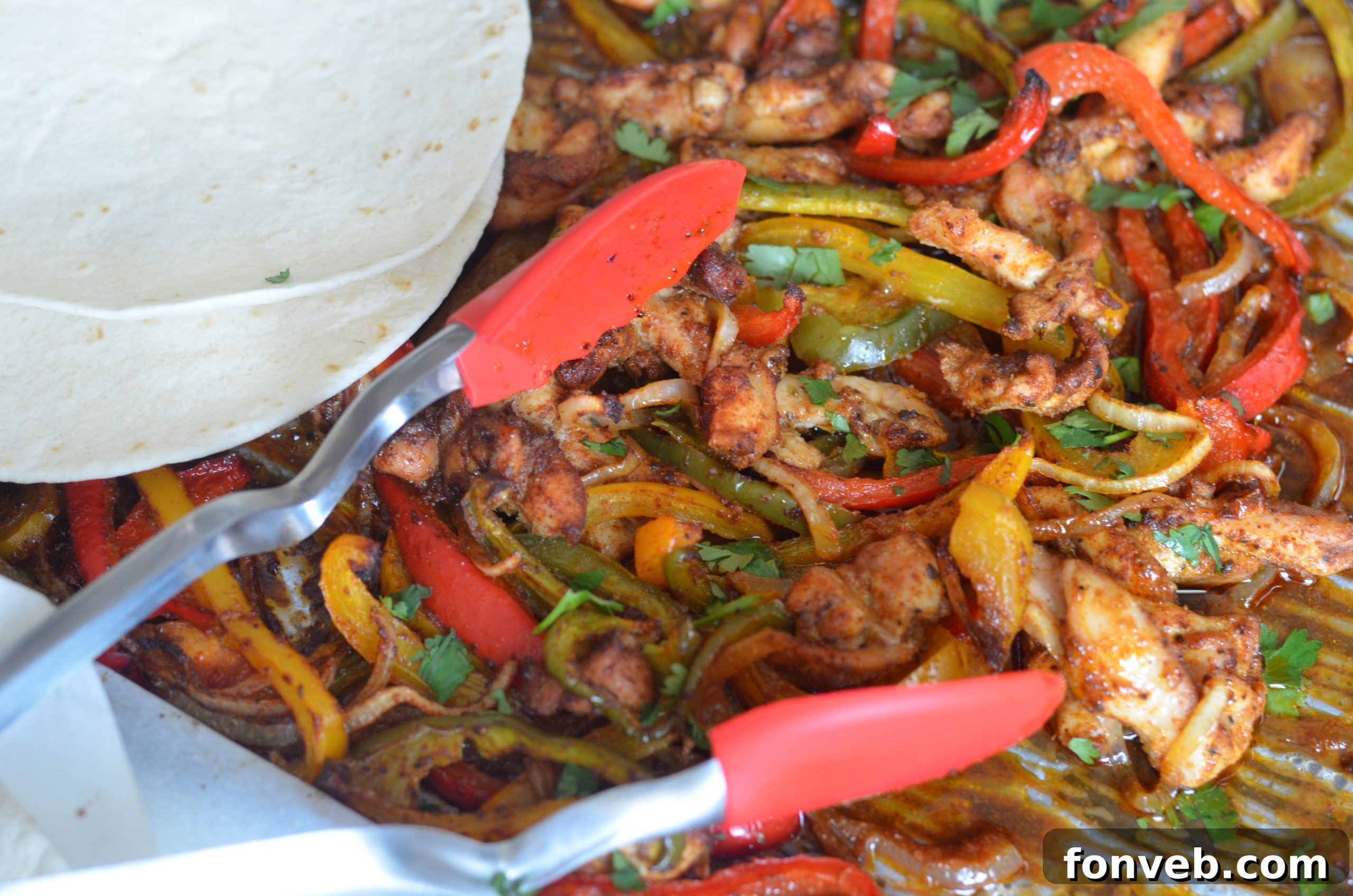 Detailed shot of marinated chicken and sliced vegetables on a sheet pan before baking.