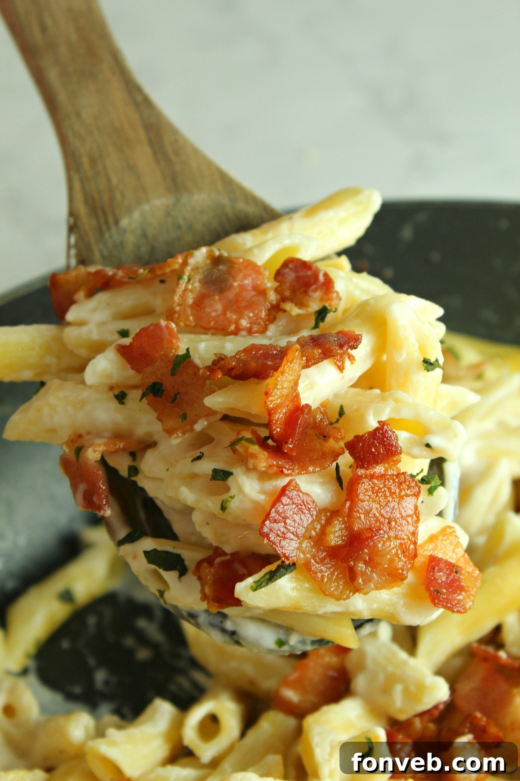 Close-up of creamy bacon alfredo pasta being tossed in a skillet, showing the rich sauce coating the penne pasta.