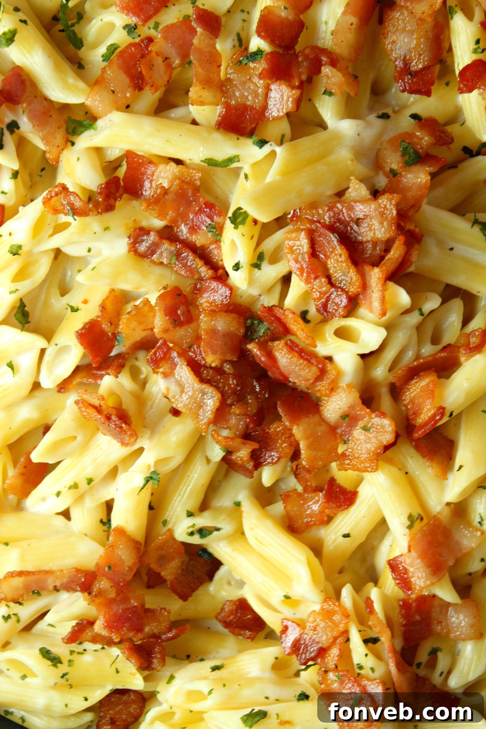 A serving of creamy bacon alfredo pasta in a bowl, with a fork ready to scoop, highlighting the crisp bacon pieces.