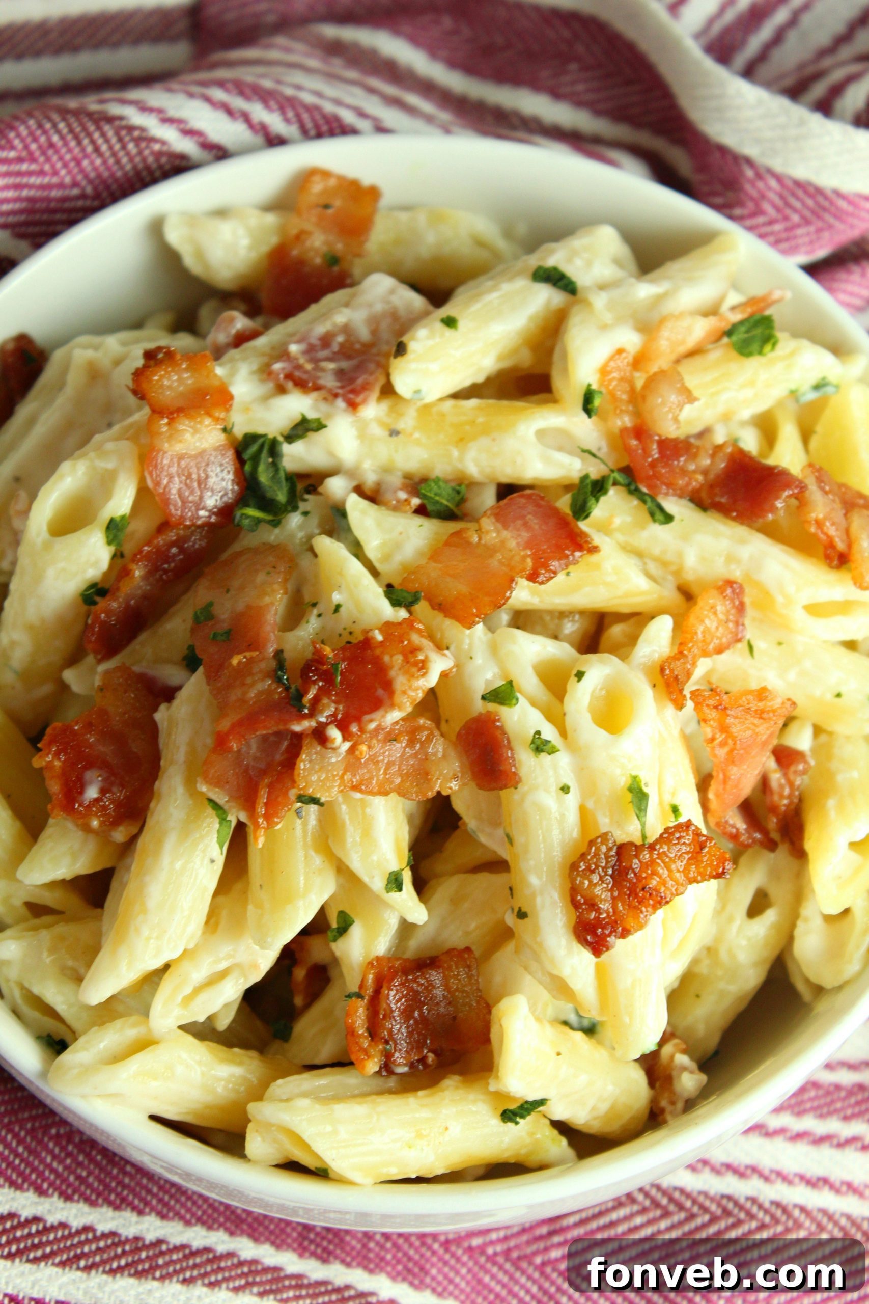 A closer view of the creamy bacon alfredo pasta in a white bowl, showing the texture of the sauce and grated Parmesan.