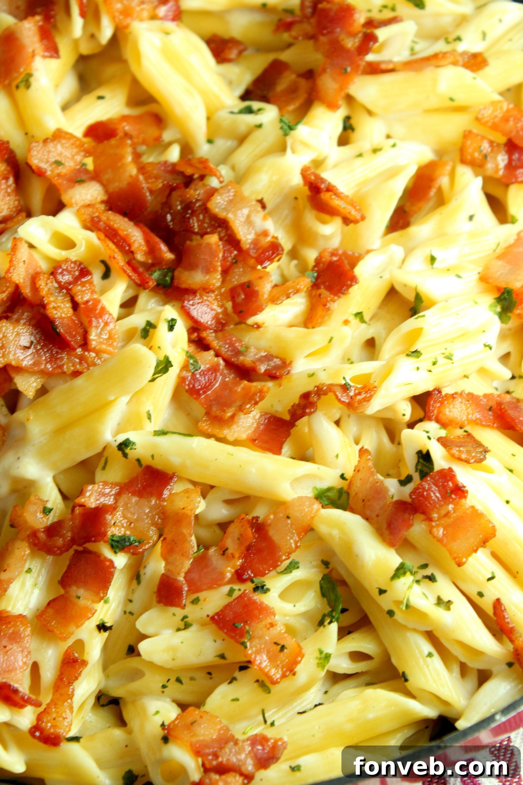 An overhead shot of a single serving of creamy bacon alfredo pasta garnished with fresh basil.
