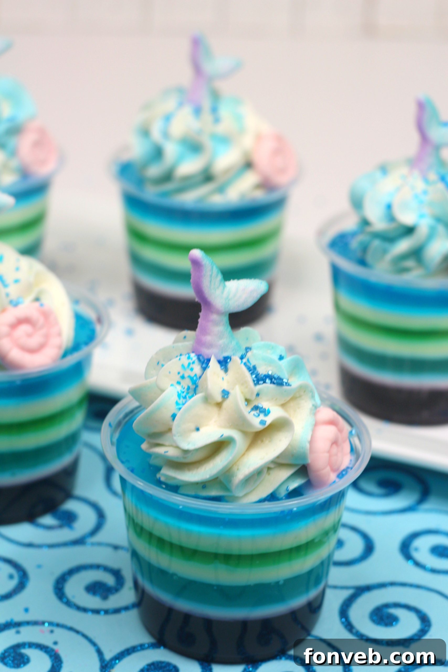 Side view of two shot glasses filled with multi-layered Mermaid Jello Shots, showcasing the clear separation of purple, white, and blue layers.
