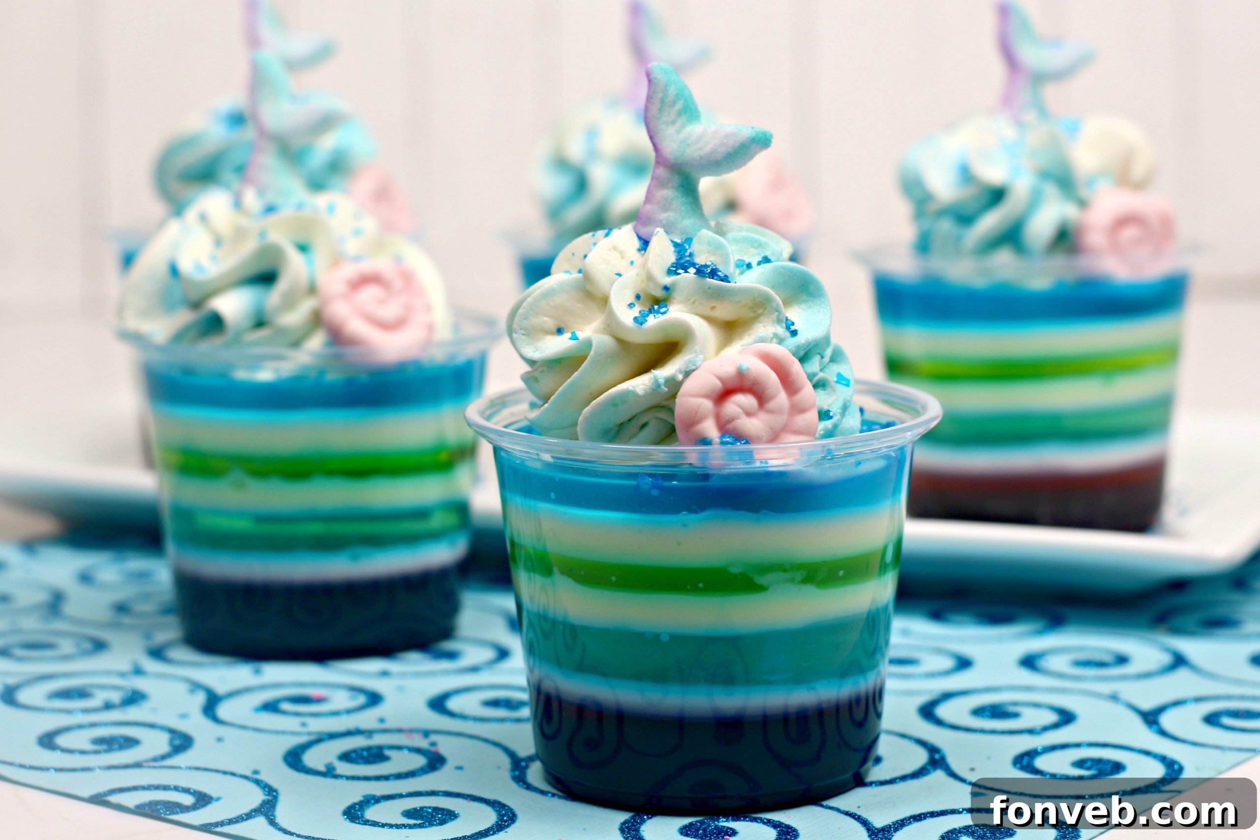 A top-down view of Mermaid Jello Shots with blue whipped cream, sprinkles, and decorative mermaid tails and seashells, arranged attractively.