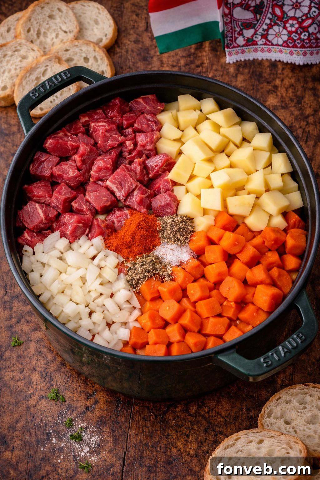 Fresh ingredients for Hungarian Goulash, including diced beef, onions, carrots, and potatoes, neatly arranged in a green Dutch oven before cooking begins.