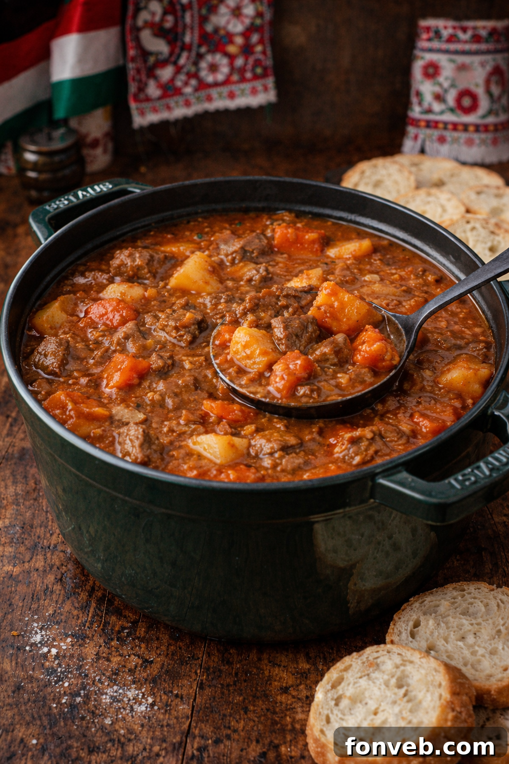 A generous serving of rich Hungarian Goulash being scooped from a green Dutch oven, showcasing its tender beef and vibrant vegetables.