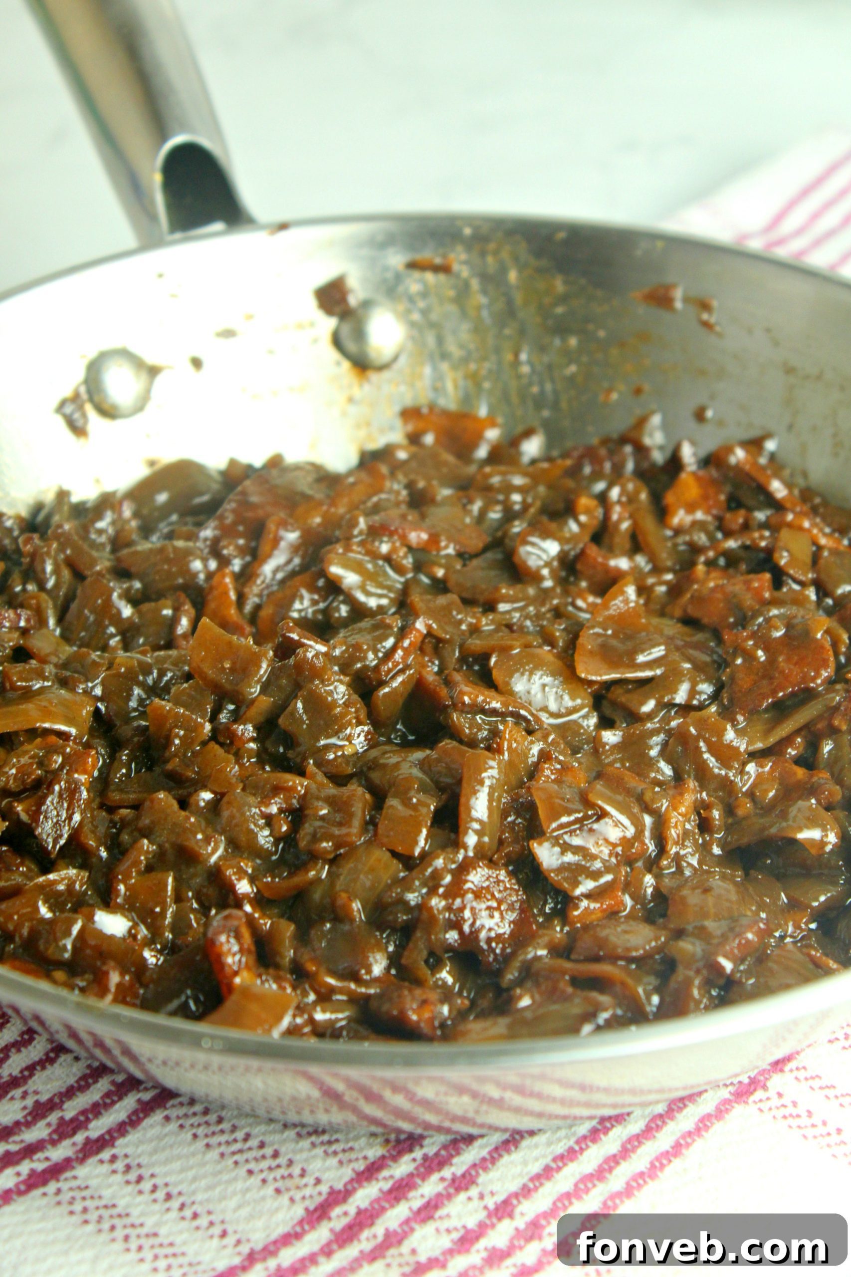 A glass jar filled with luscious, dark brown bacon jam, garnished with fresh herbs, sitting on a rustic wooden surface.