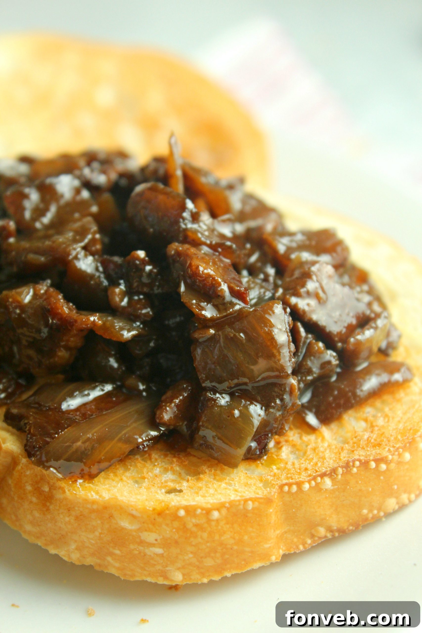 Three glass mason jars filled with bacon jam, lined up on a wooden surface, ready for storage.