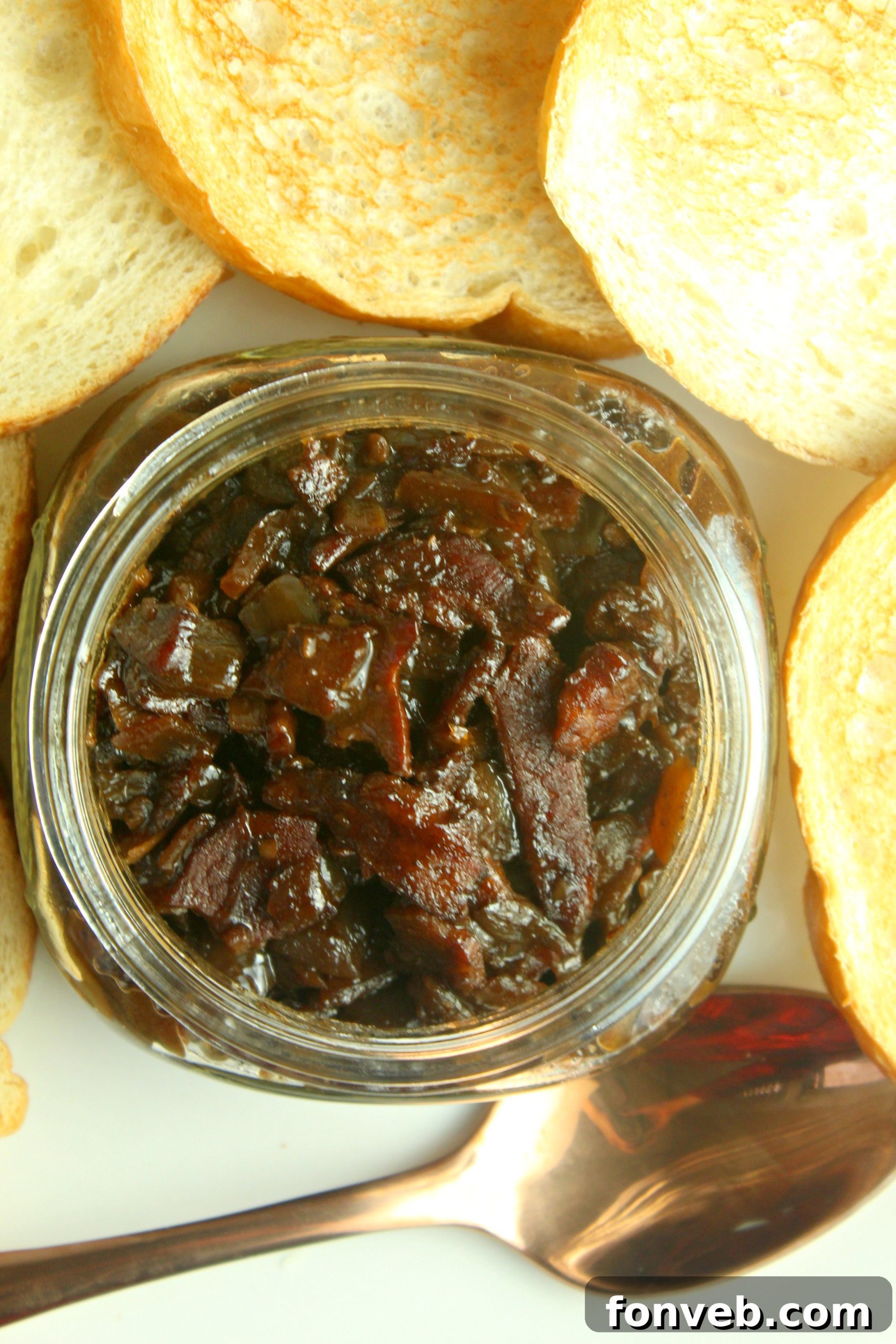 Close-up shot of chopped onions and bacon sizzling in a heavy skillet during the initial cooking phase of bacon jam.