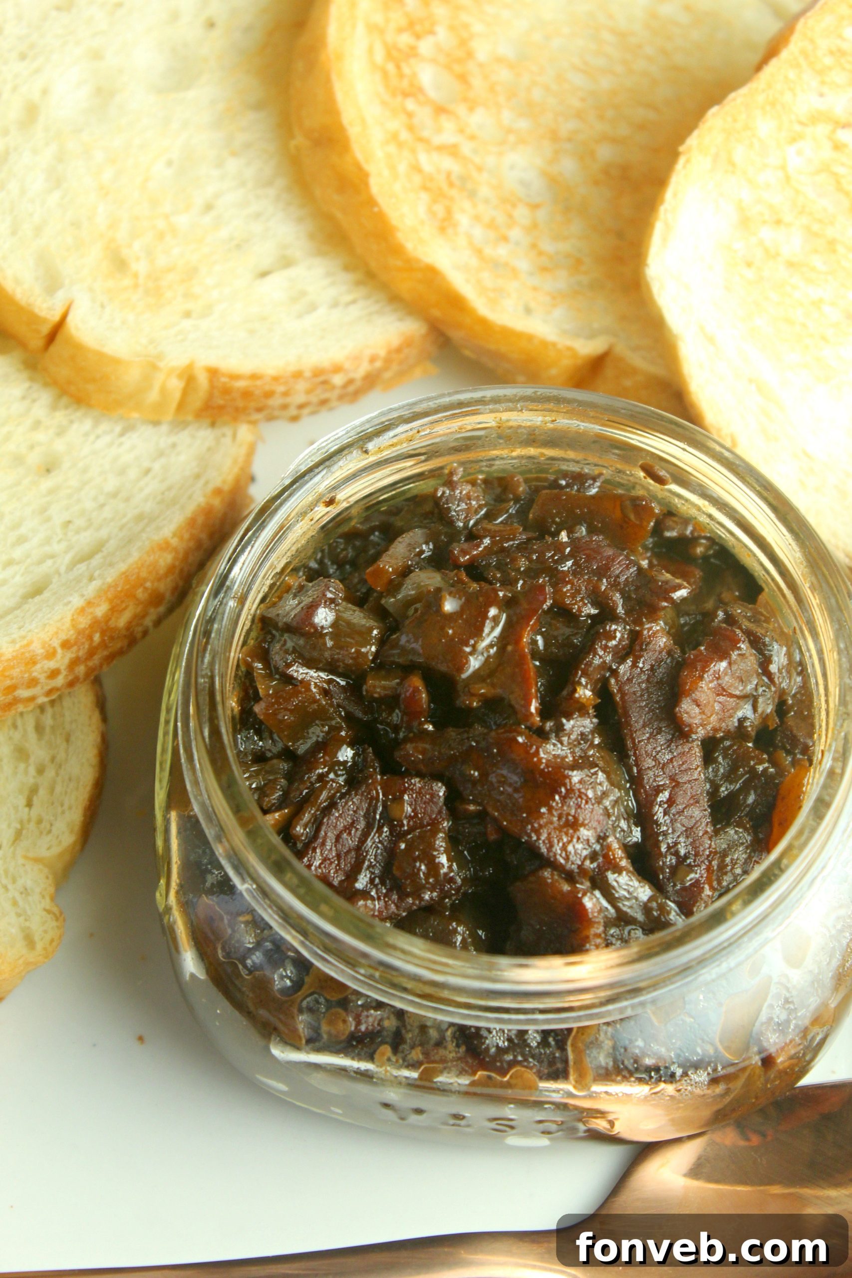 Freshly made bacon jam, still warm, being spooned into small glass jars for storage or gifting.