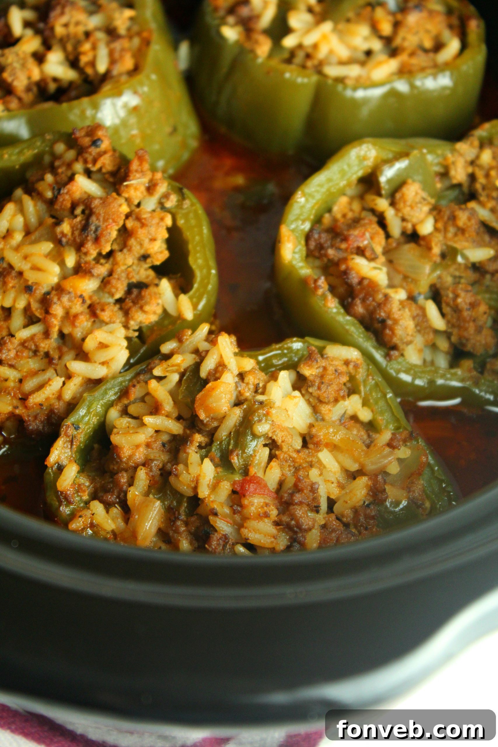 Close-up of three perfectly cooked Slow Cooker Stuffed Peppers, rich with a savory beef and rice filling, nestled in a vibrant tomato sauce.