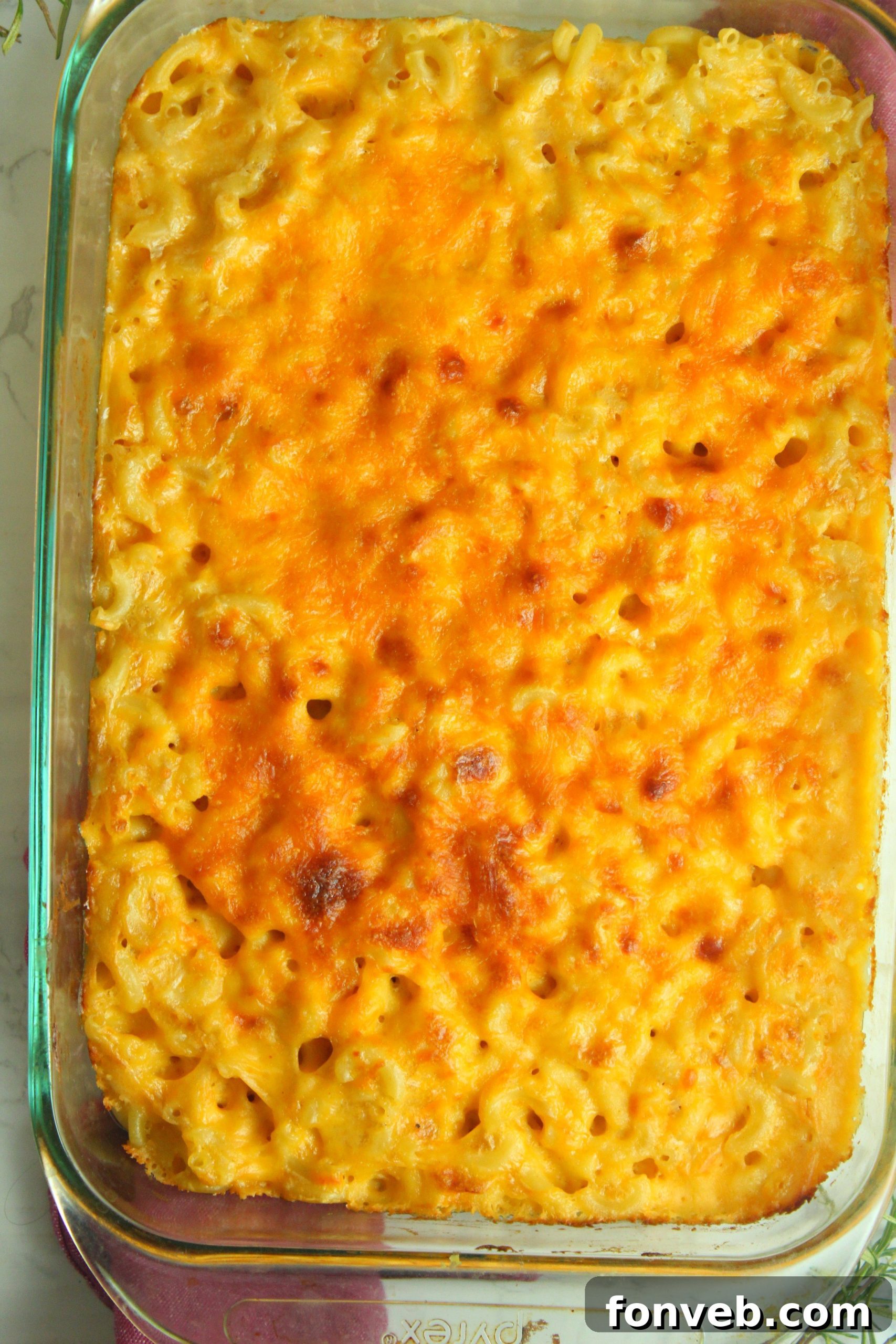 A generous serving of Southern Baked Macaroni & Cheese in a white baking dish, ready to be served, highlighting its rich, golden-brown crust.