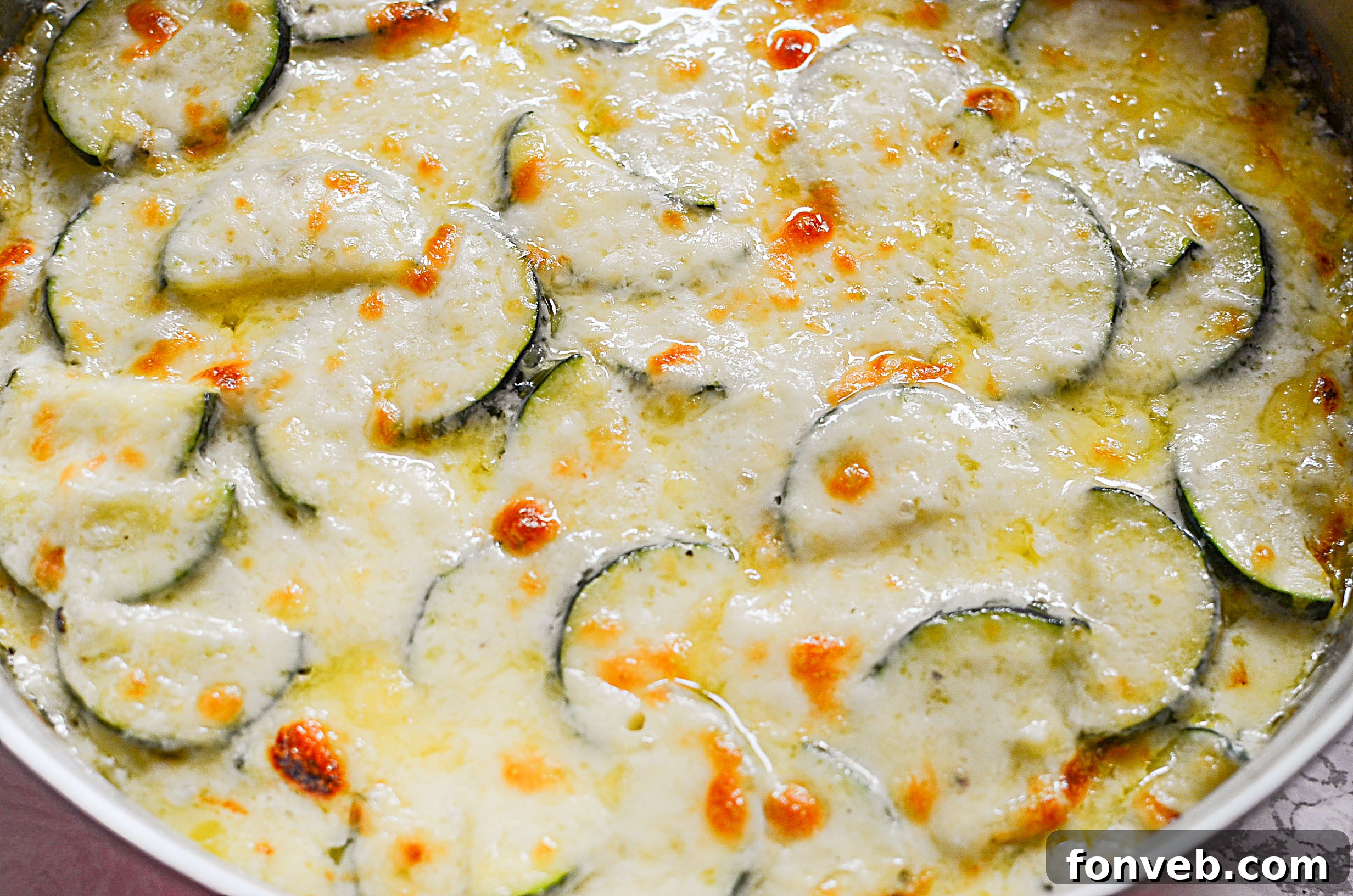Close-up view of the bubbling, golden-brown cheese topping on the hot Cheesy Zucchini Gratin