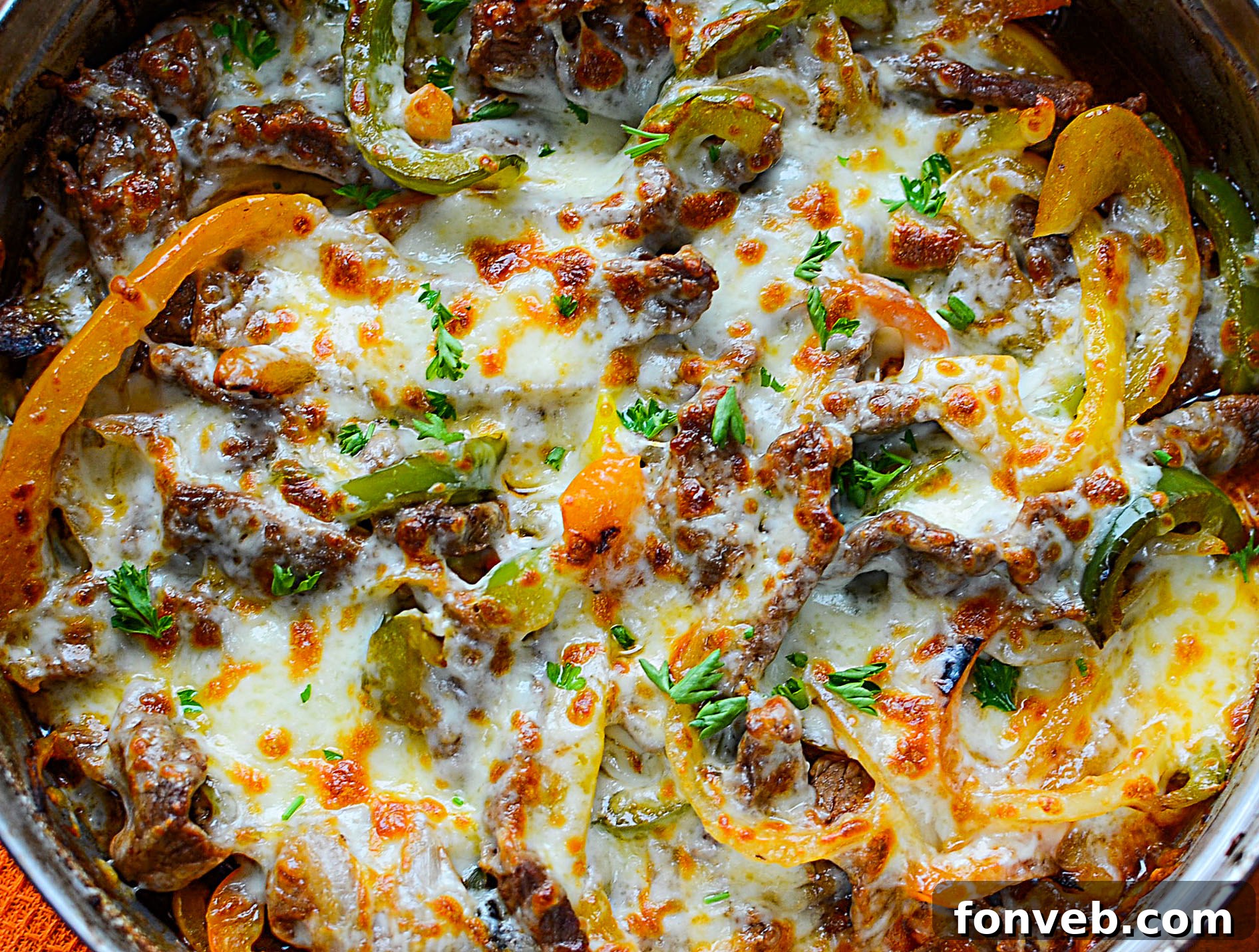 A skillet full of cooked steak, sliced onions, and bell peppers, topped with generous slices of melting cheese.