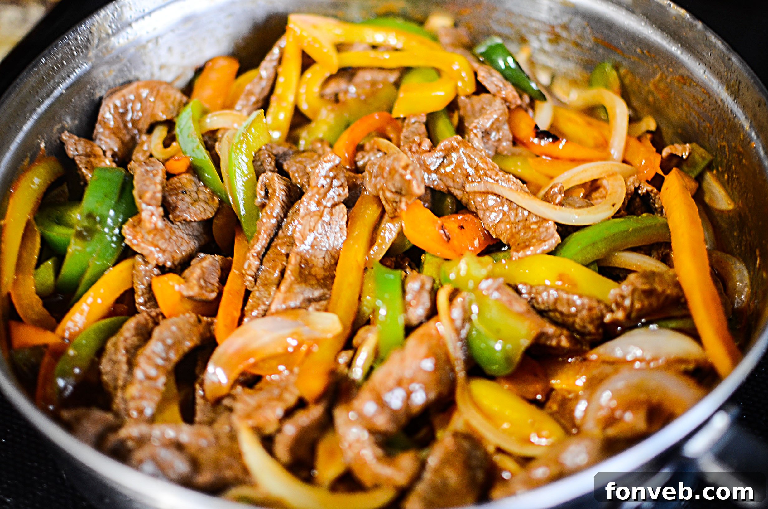 A close-up view of the ingredients cooking in a skillet, showing the steak browning with onions and peppers.