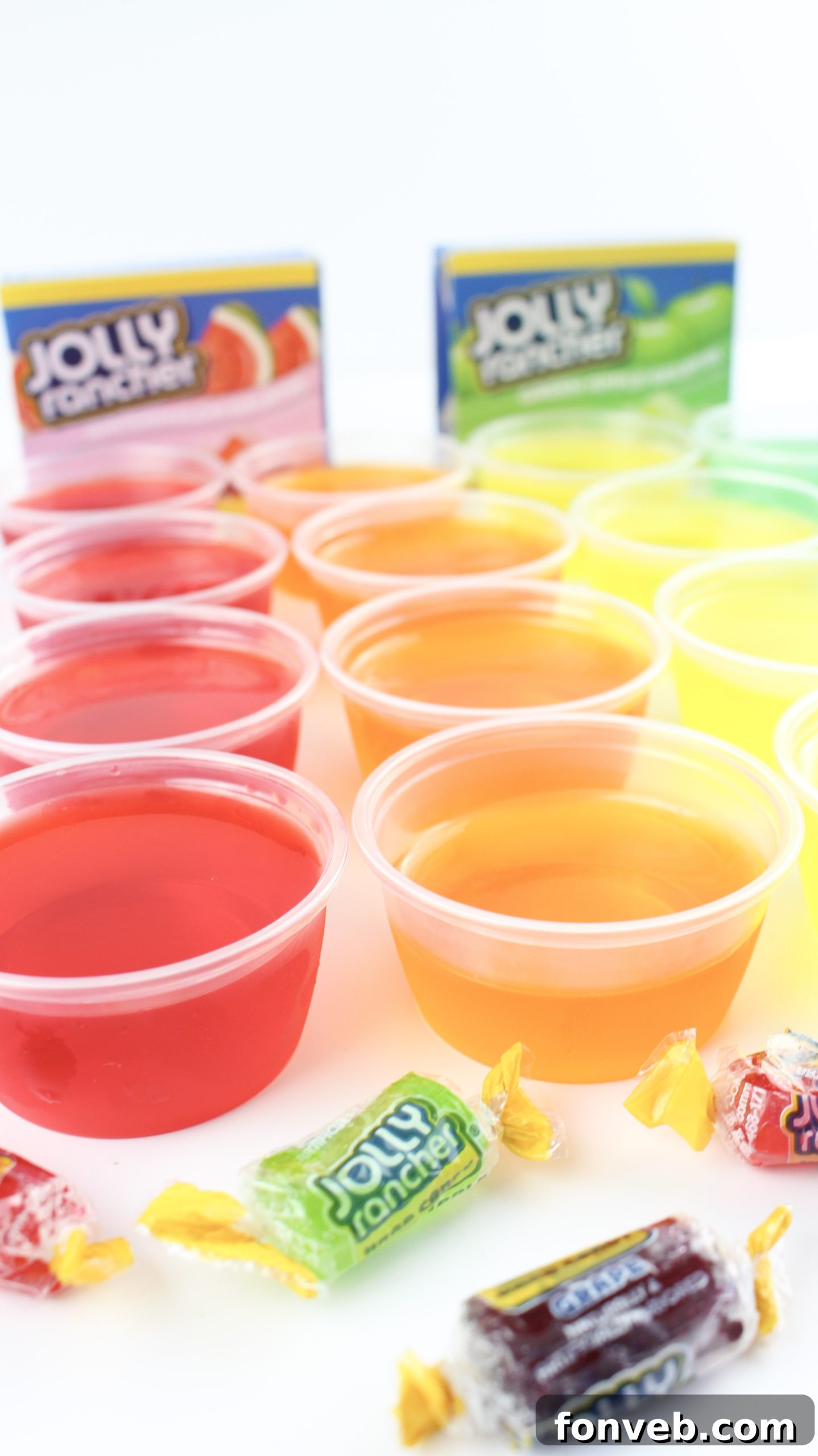 A close-up of several Jello shots, including green apple and blue raspberry, in a casual party setting.