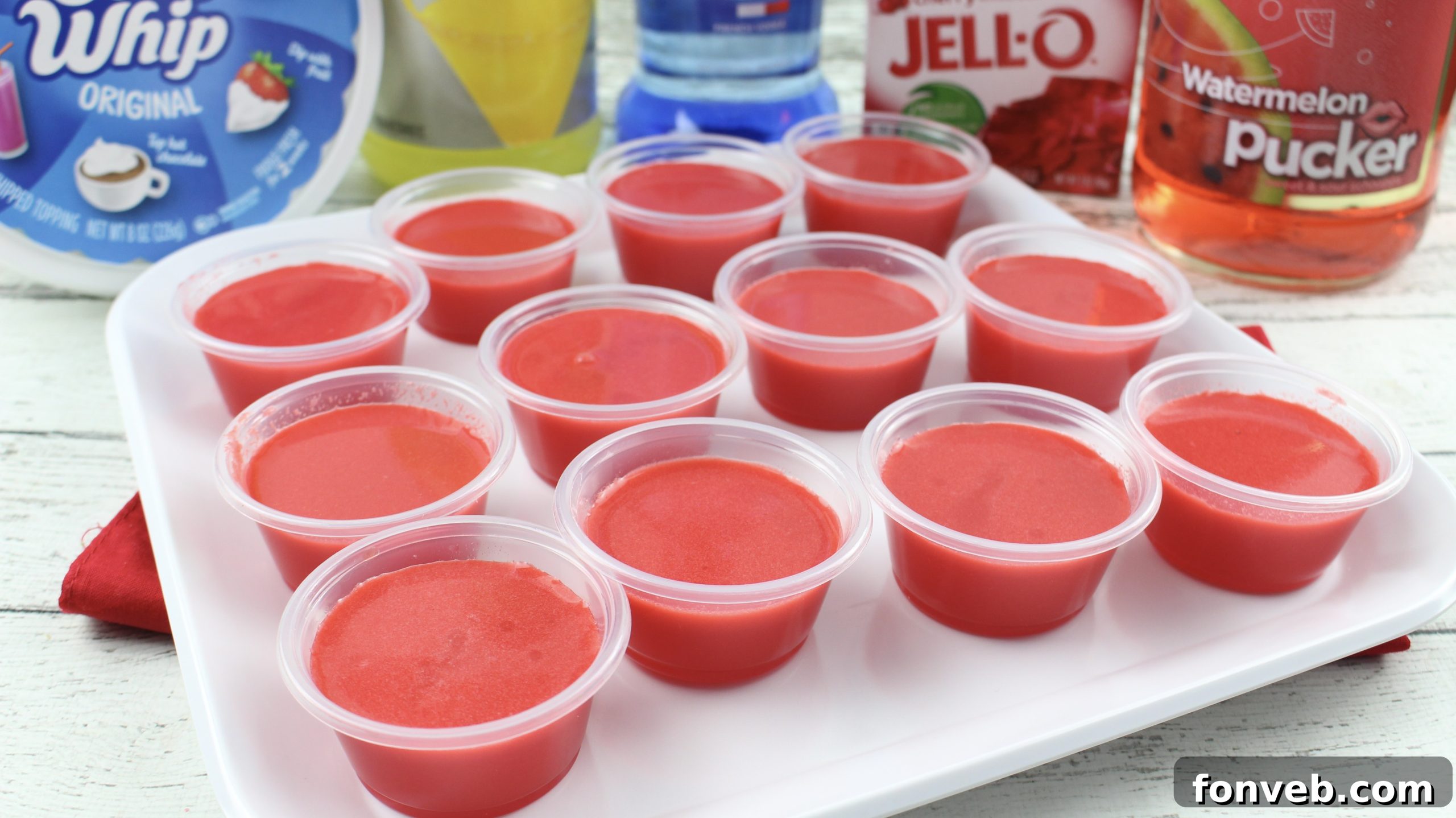 Close-up of a single Cherry Starburst Jell-O Shot, topped with a dollop of whipped cream and a candy.