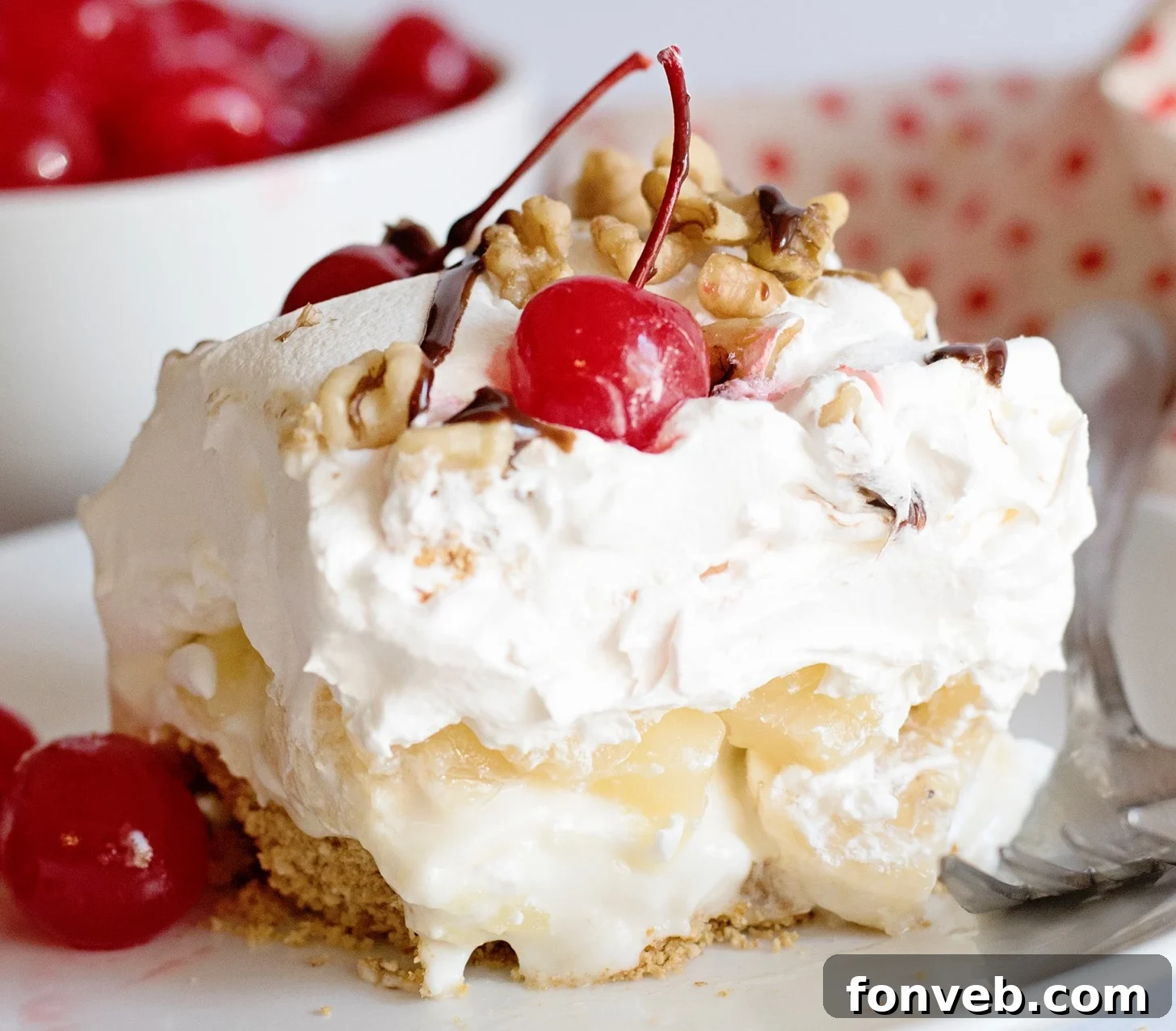 No Bake Banana Split Dream 2 Close-up of a luscious No-Bake Banana Split Dessert, showcasing its vibrant layers of bananas, pineapple, whipped cream, and cherries on a graham cracker crust.