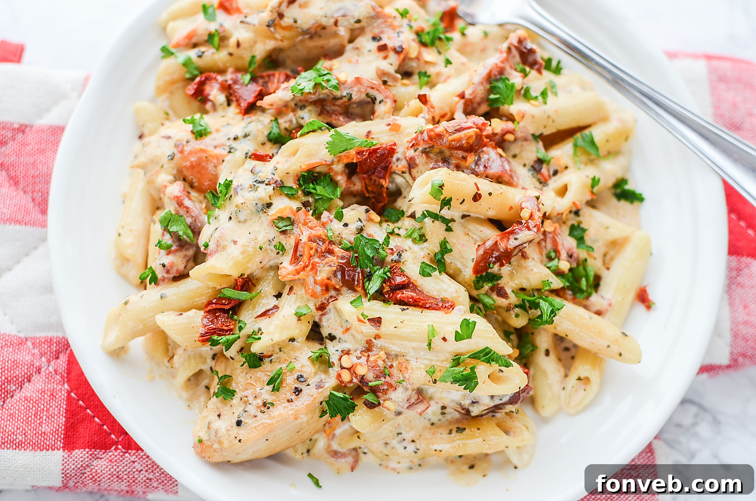A close-up of the chicken pieces and sun dried tomatoes covered in the creamy sauce before mixing with pasta.