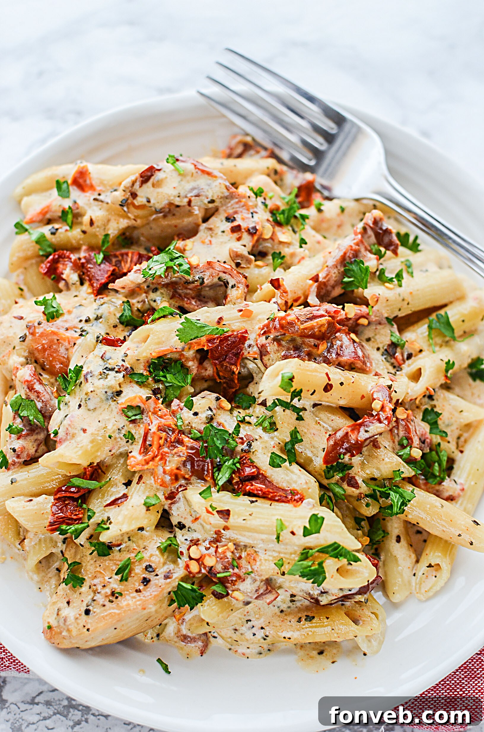 Cooked pasta being added to the creamy sun dried tomato sauce in a large skillet.