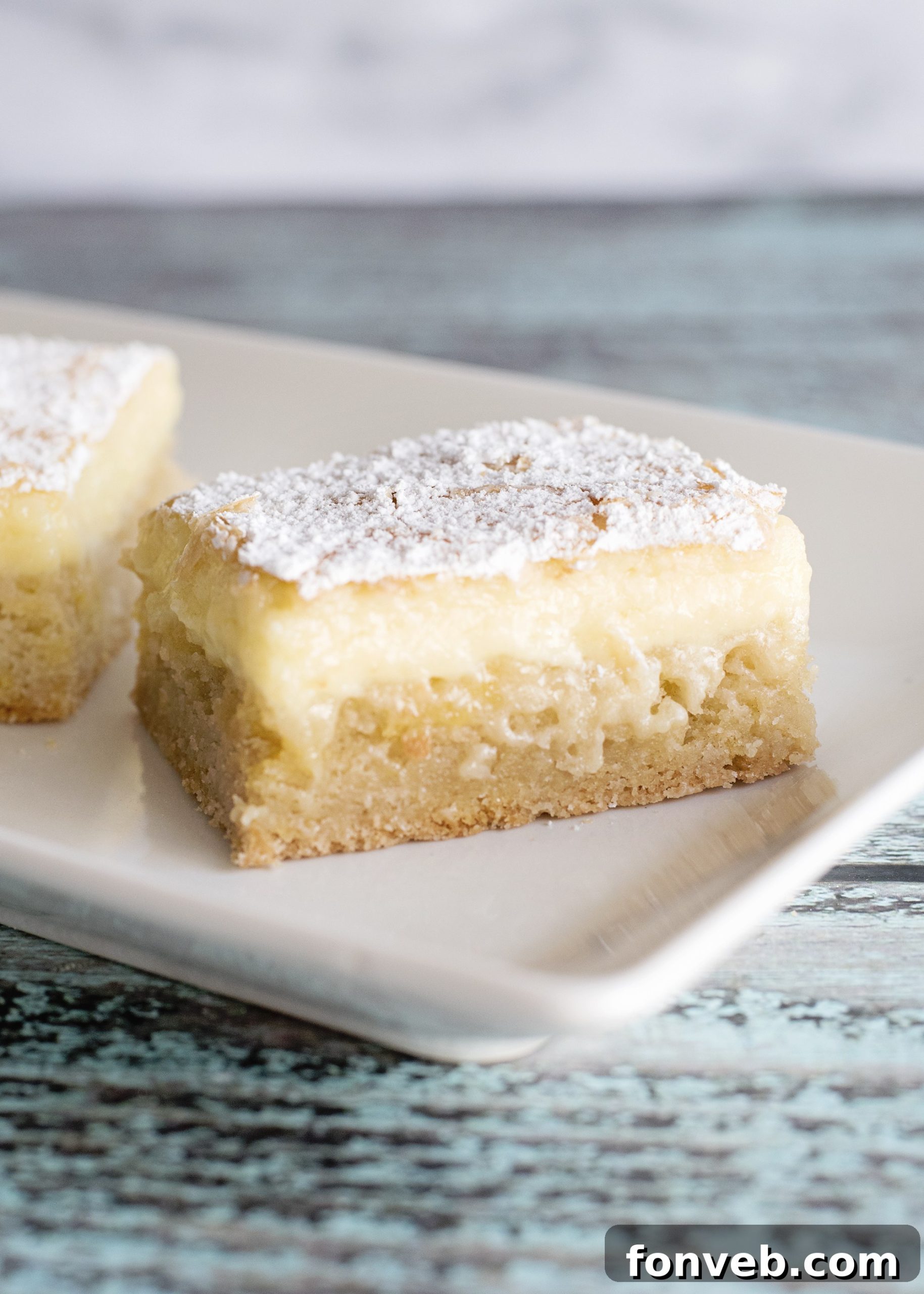 Several Ooey Gooey Butter Bars cooling on a wire rack after being baked, showing the soft center.
