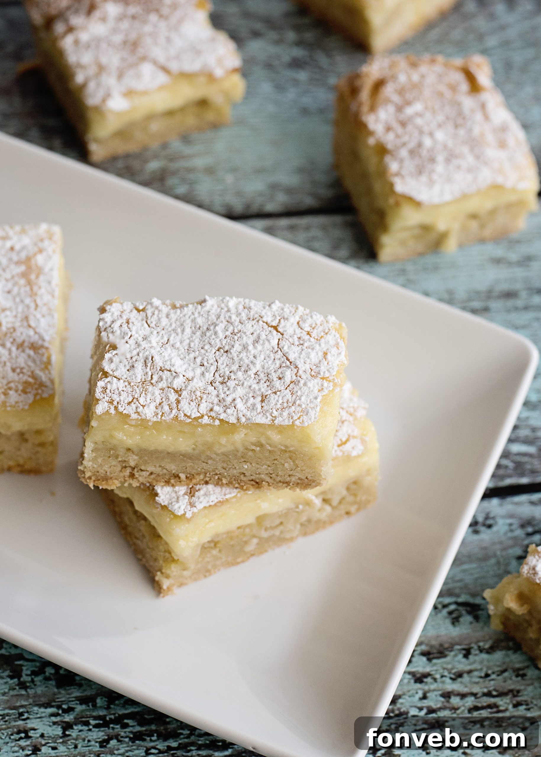 Overhead shot of many Ooey Gooey Butter Bars arranged on a rustic wooden surface, dusted with powdered sugar.