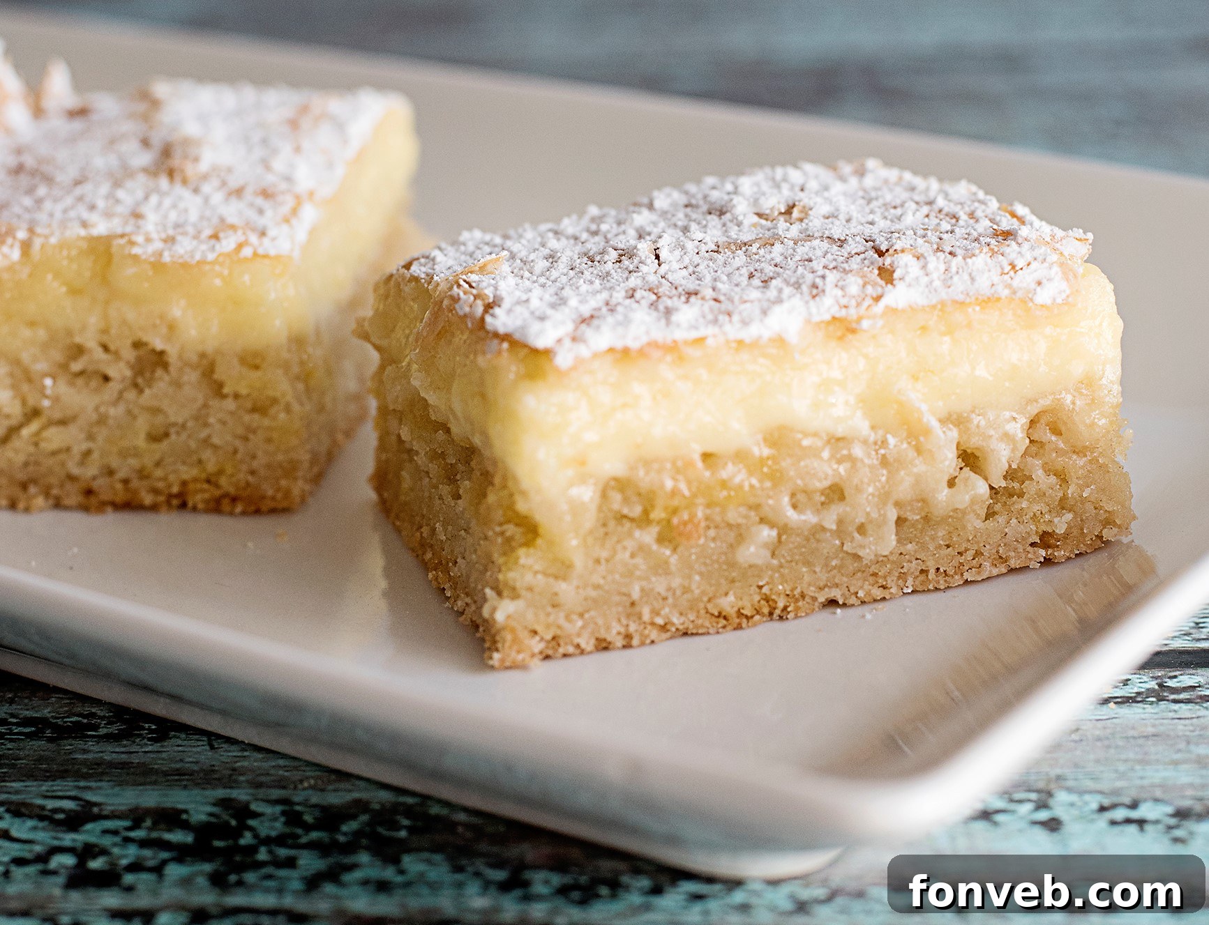 A close-up of a single Ooey Gooey Butter Bar on a white plate, showing its cross-section and gooey interior.