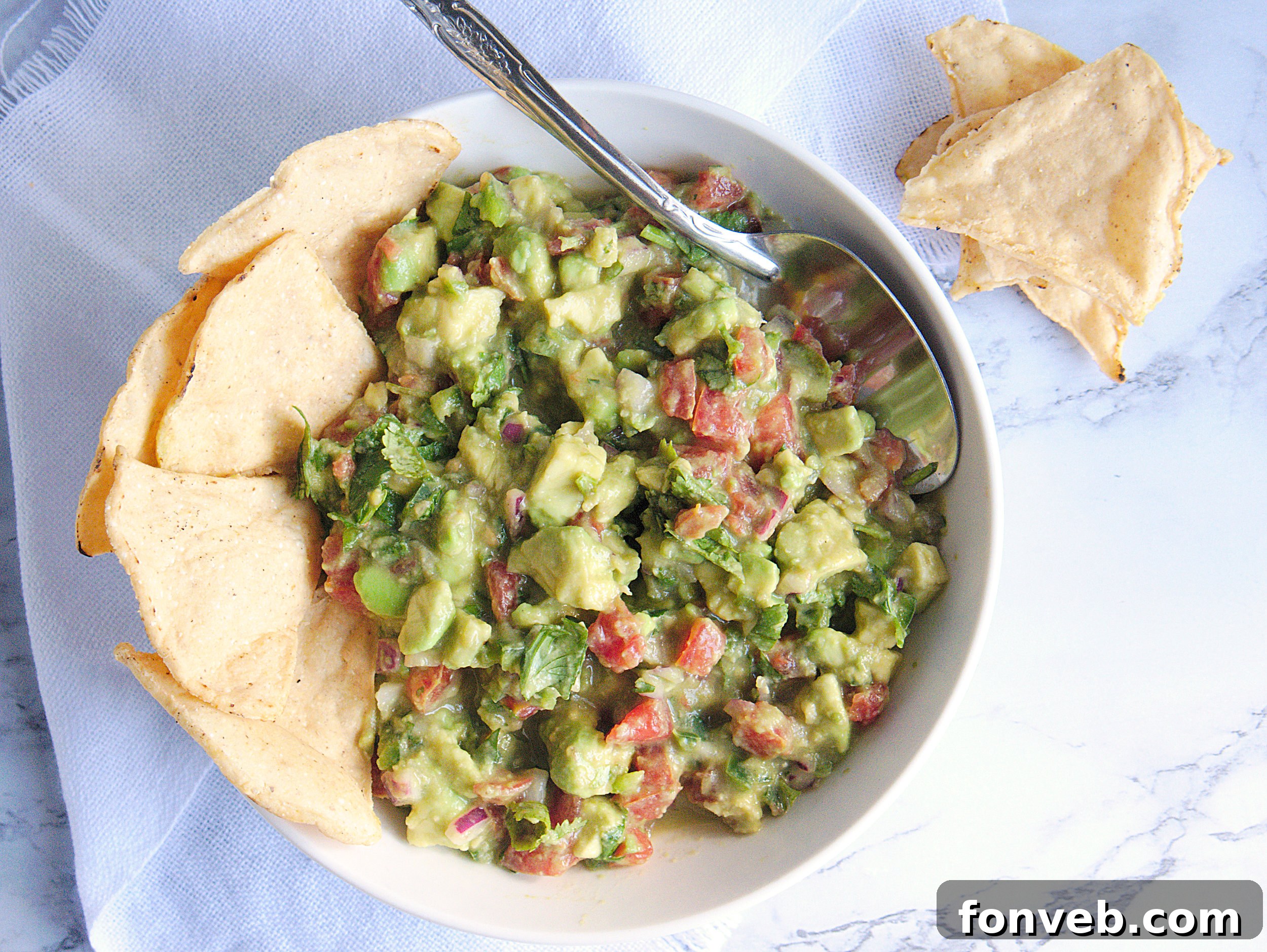 A close-up of a serving of chunky guacamole with tortilla chips, ready for a party.