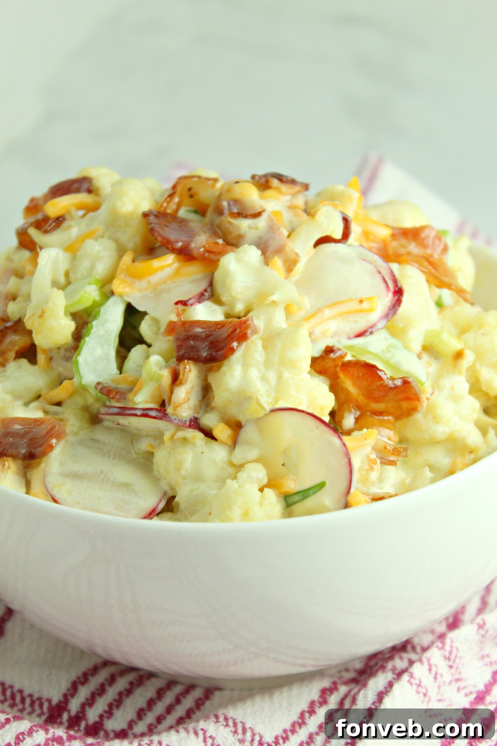 Two hands mixing the cauliflower salad in a large glass bowl