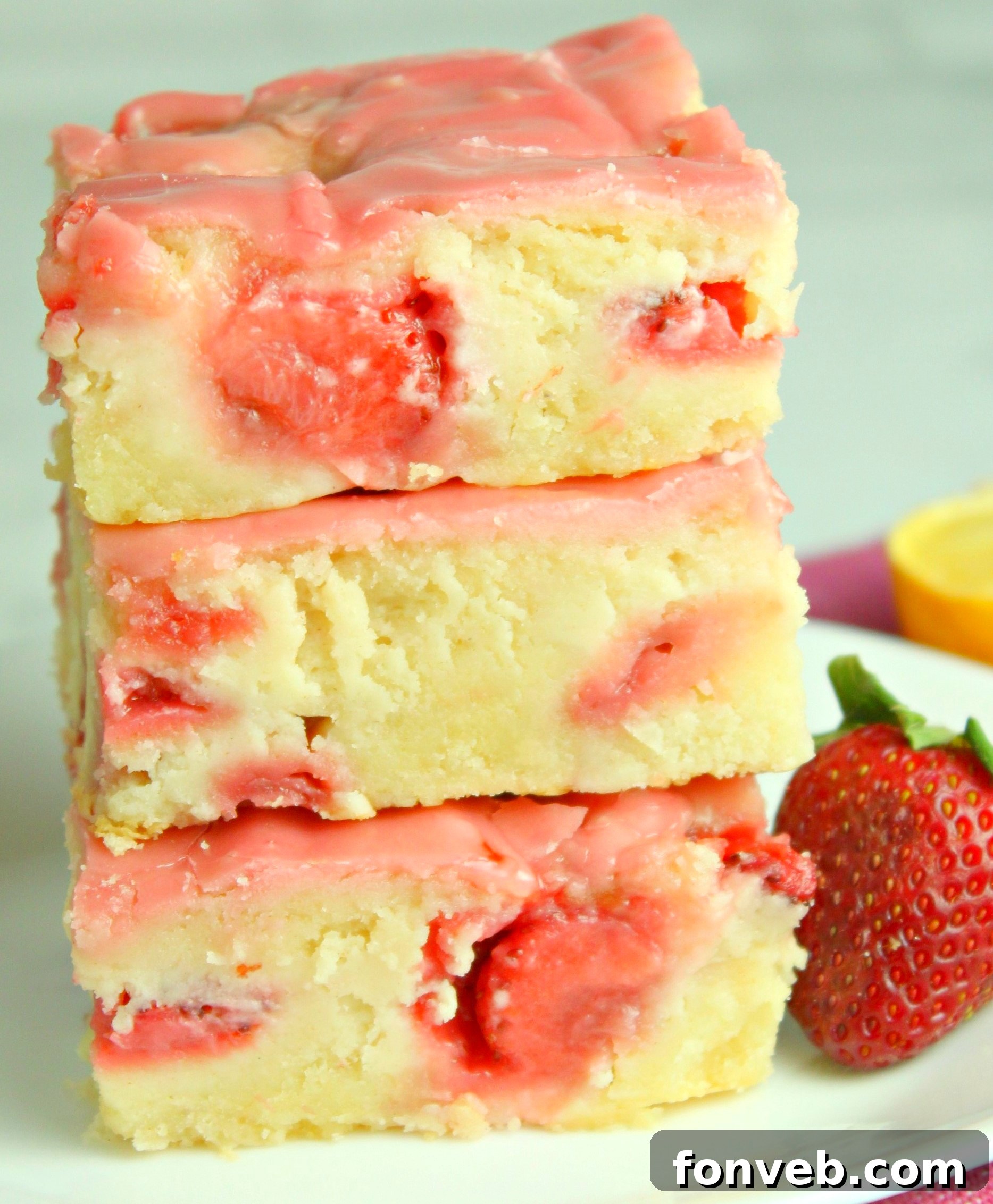 Close-up of baked strawberry lemon blondies with a light pink icing, garnished with fresh strawberry slices, sitting on a white tray.